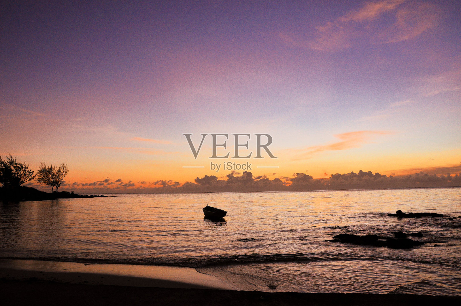 美丽的大海，一艘小船在上面航行，天空的背景被日落所染照片摄影图片