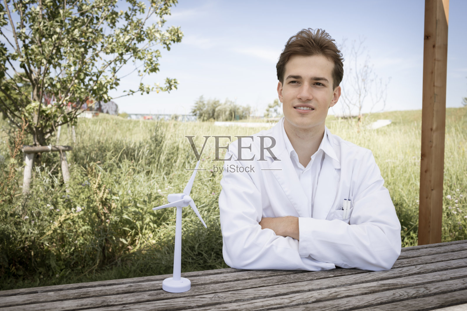 年轻的科学家与风轮机模型站在大自然外，穿着白色外套照片摄影图片
