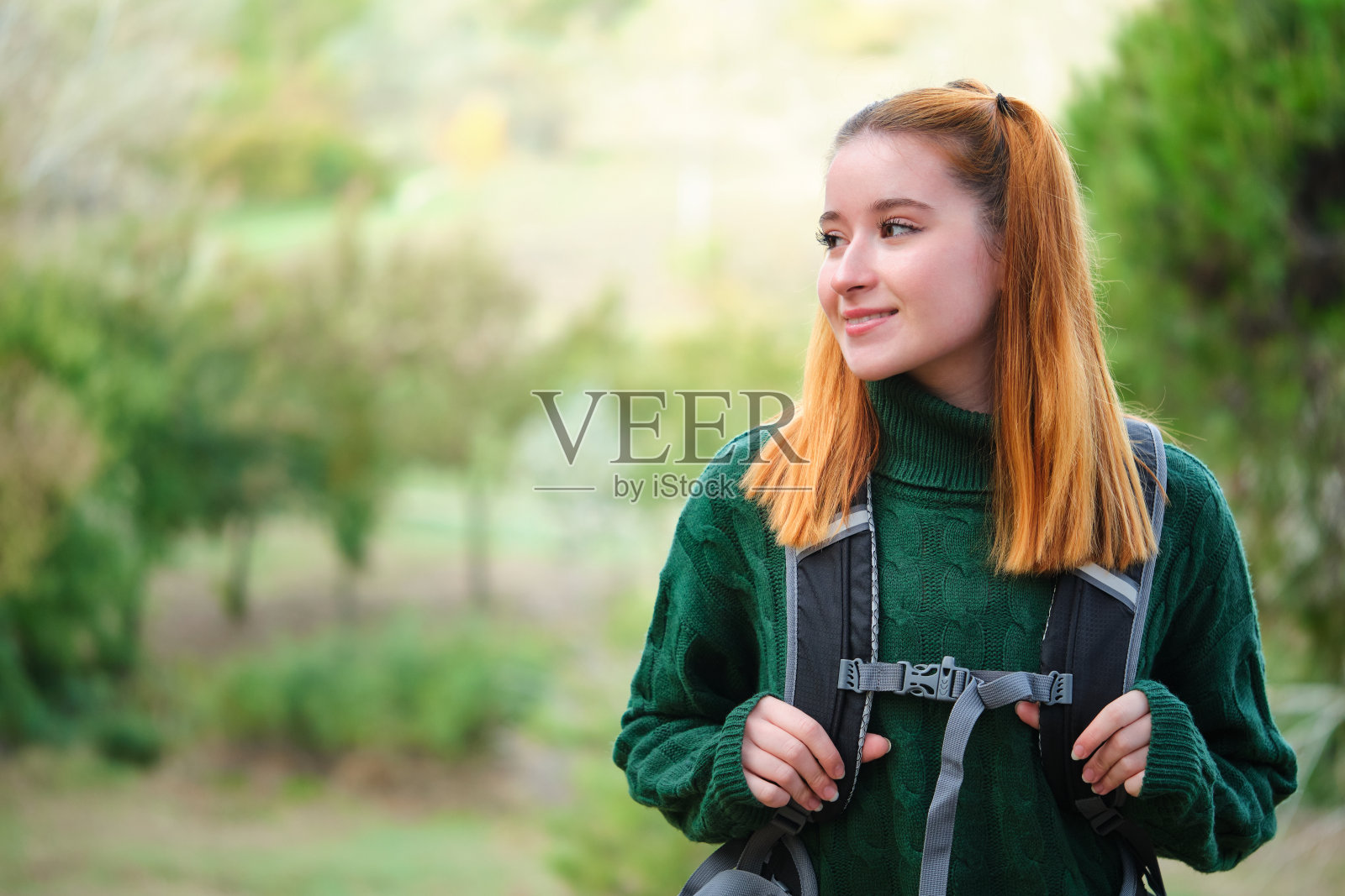 笑眯眯的徒步旅行者红发年轻女子背着背包走在山上。照片摄影图片