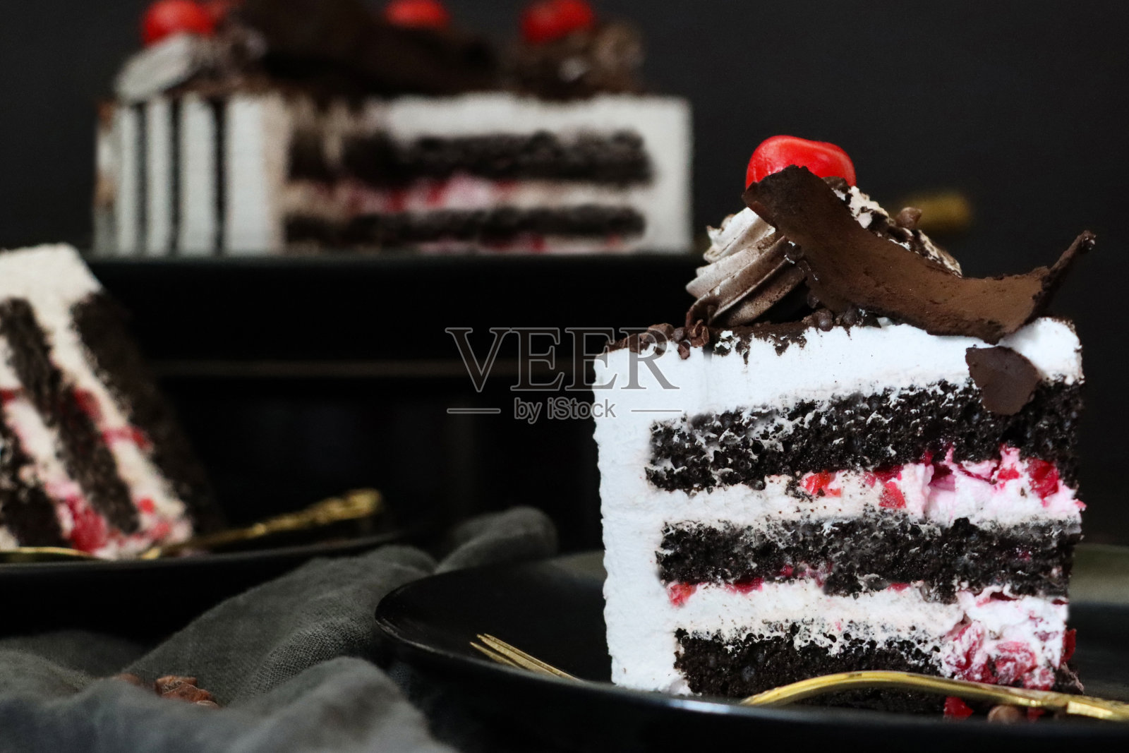 黑森林大门切片的图片，上面有莫雷罗樱桃，豪华的巧克力蛋糕上有奶油，上面覆盖着融化的巧克力，黑色背景，三层照片摄影图片