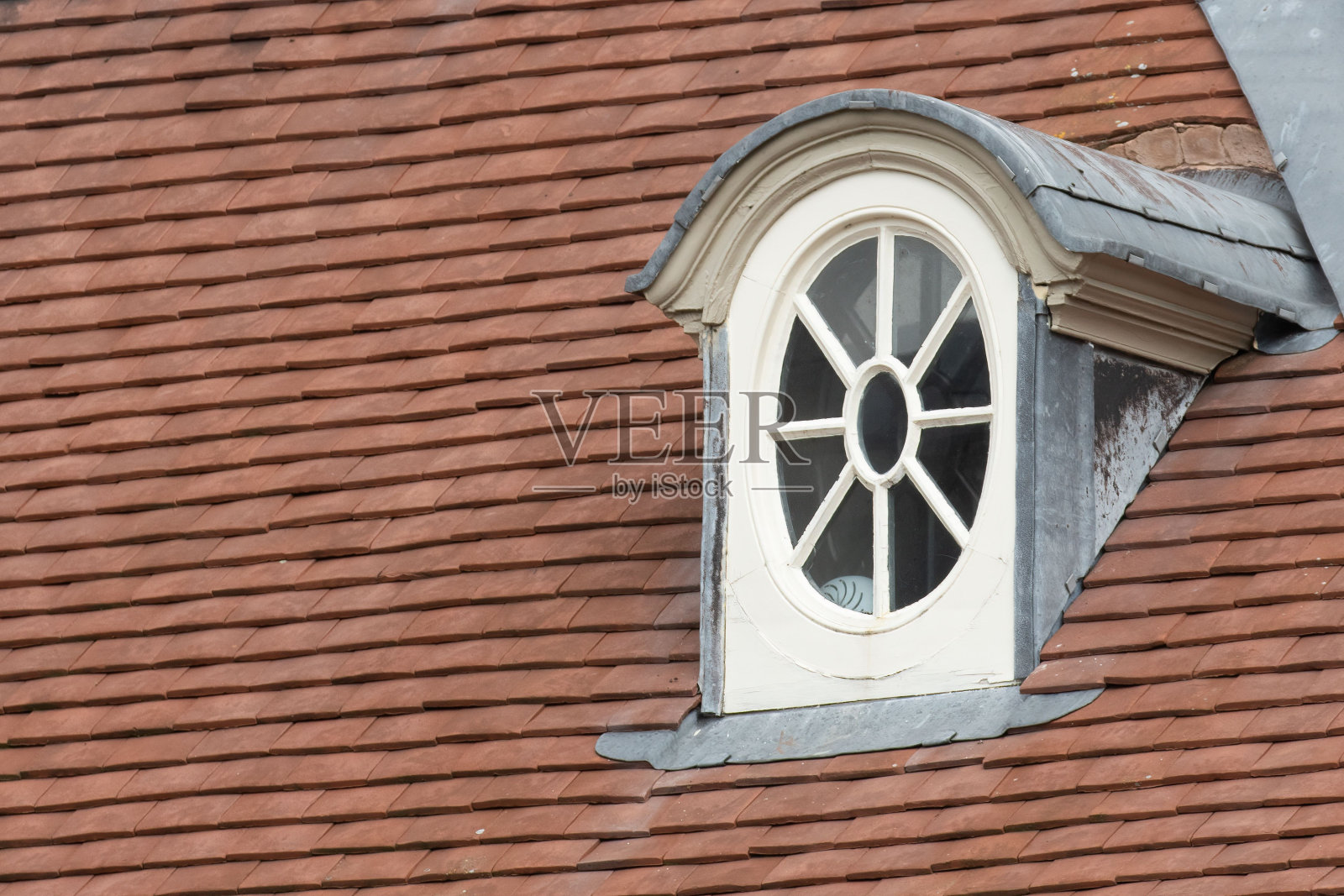 红瓦屋顶上有一扇白色木制品的圆窗照片摄影图片