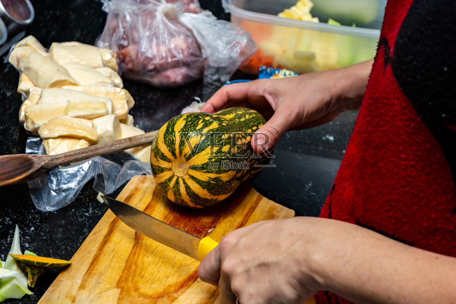 穿着红围裙的人正在切西葫芦准备晚餐照片摄影图片