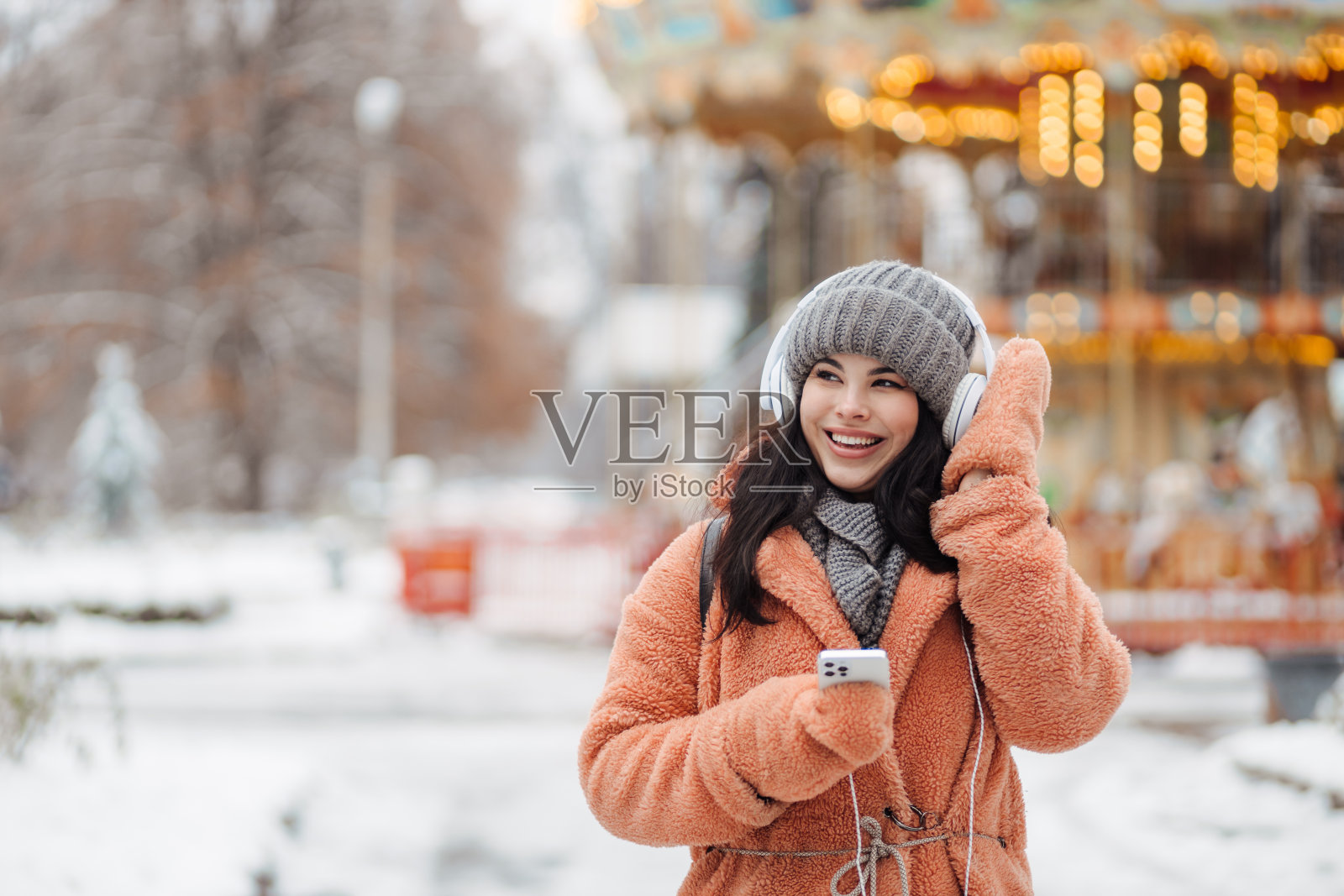 漂亮的年轻长发女子在粉红色外套享受冬天的一天和听音乐的耳机在雪公园照片摄影图片