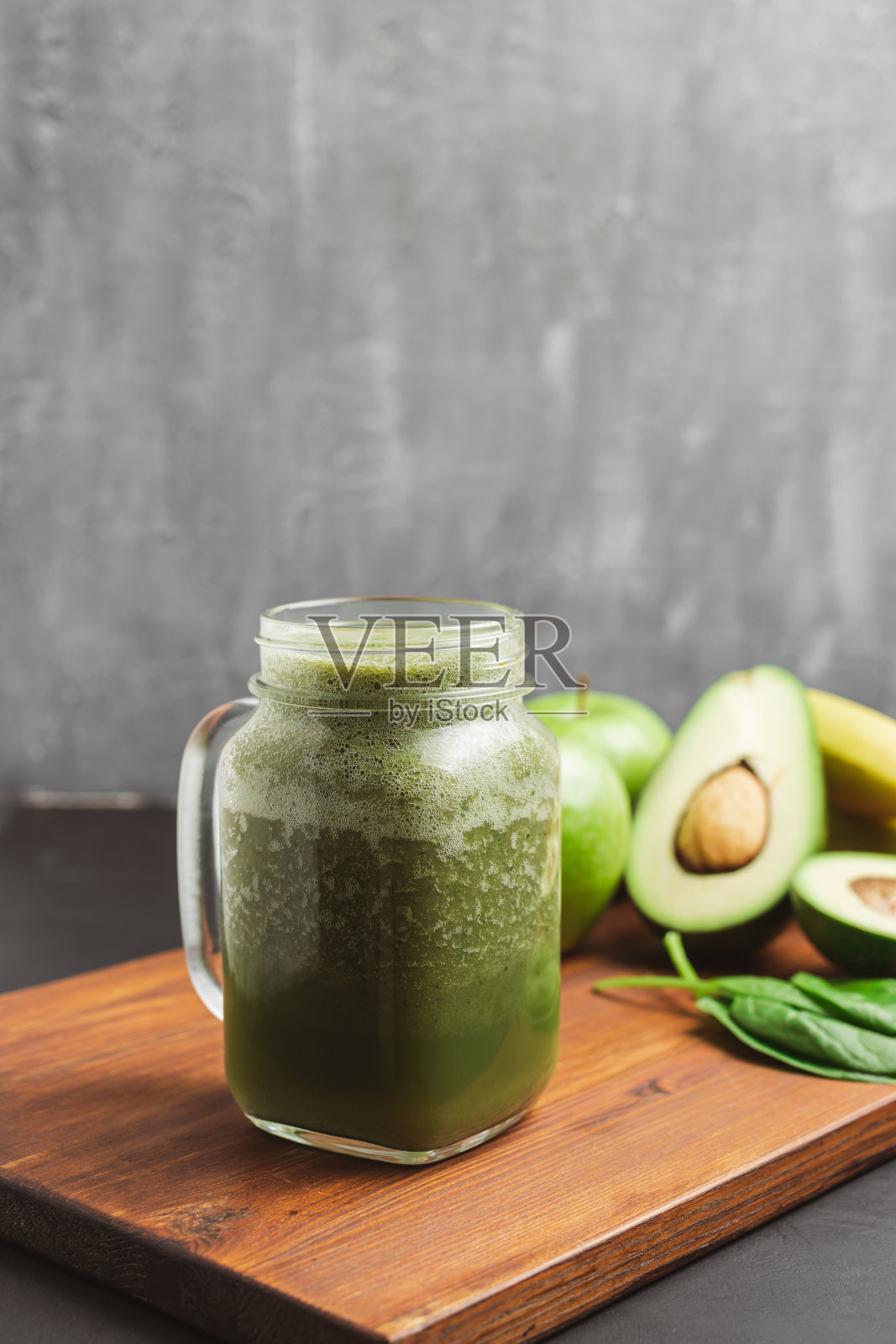 绿色冰沙饮料混合在玻璃罐中，鳄梨，菠菜叶和苹果在木板上照片摄影图片
