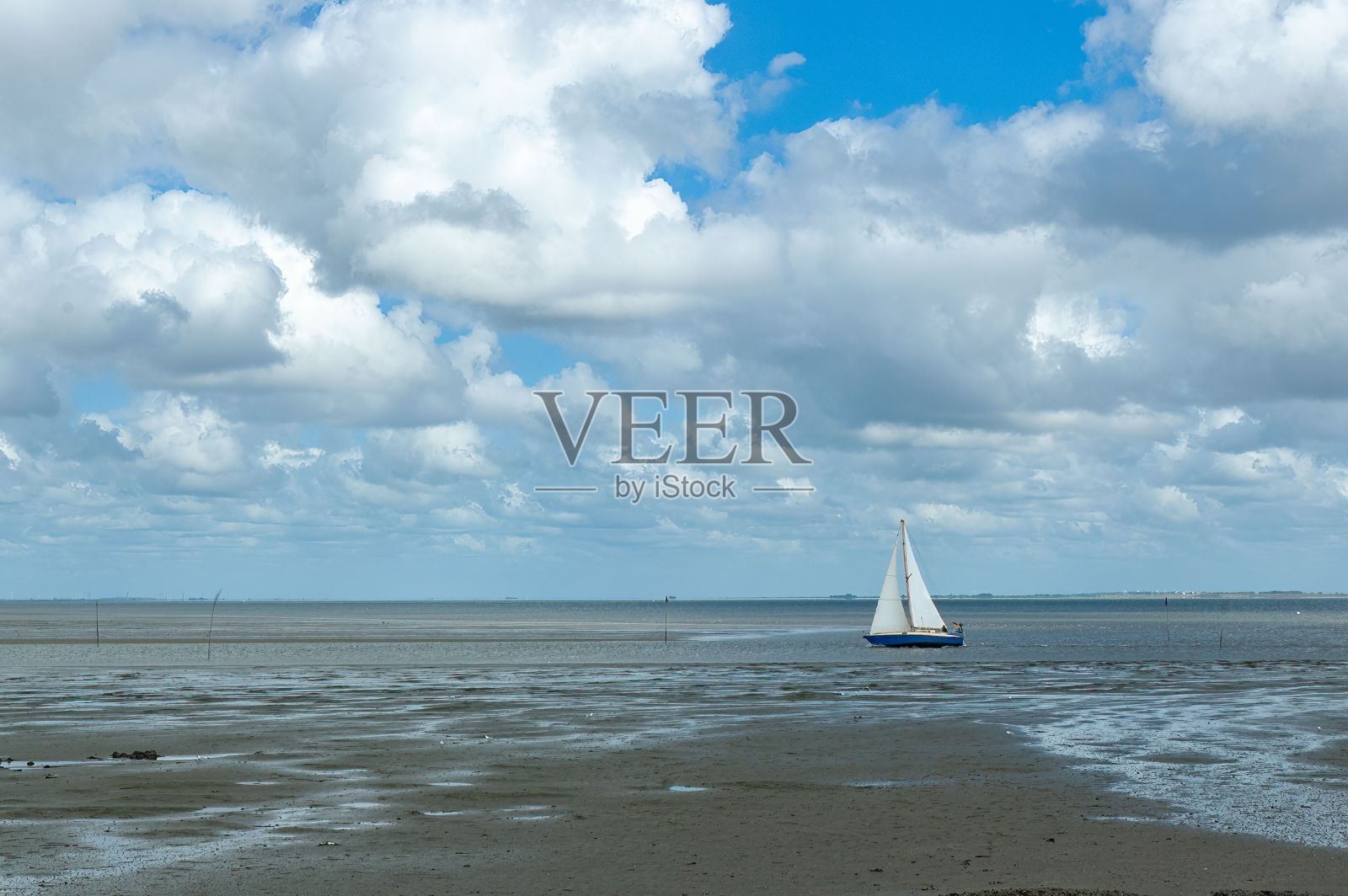 帆船从德国佩尔沃姆岛的沙滩上驶向岸边，映衬着蔚蓝多云的天空照片摄影图片