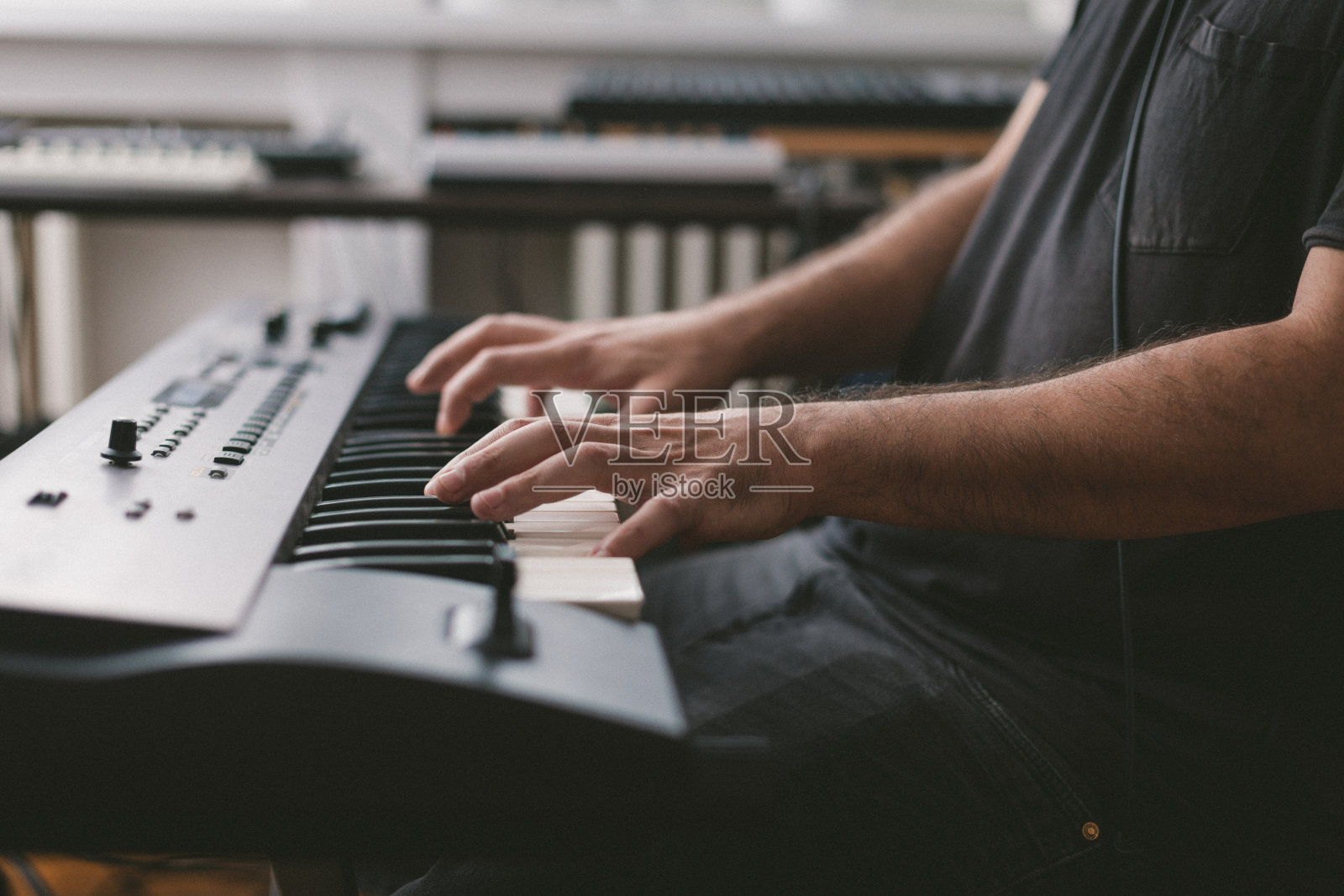 年轻人坐在家里的椅子上，戴着耳机，弹奏着电子钢琴键盘照片摄影图片