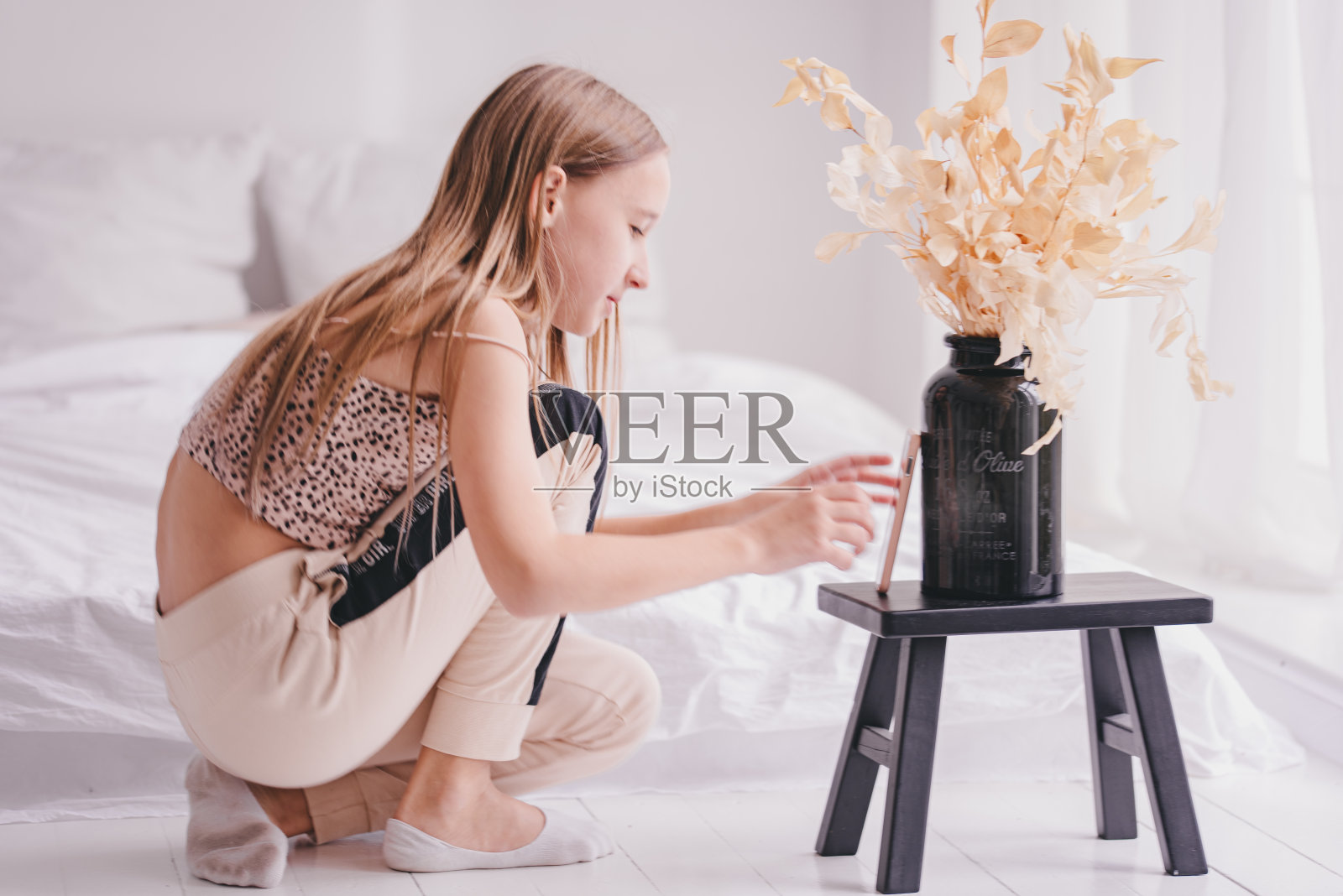 一个带着花的女孩。他摸了摸花瓶。小女孩在房间的床上照片摄影图片