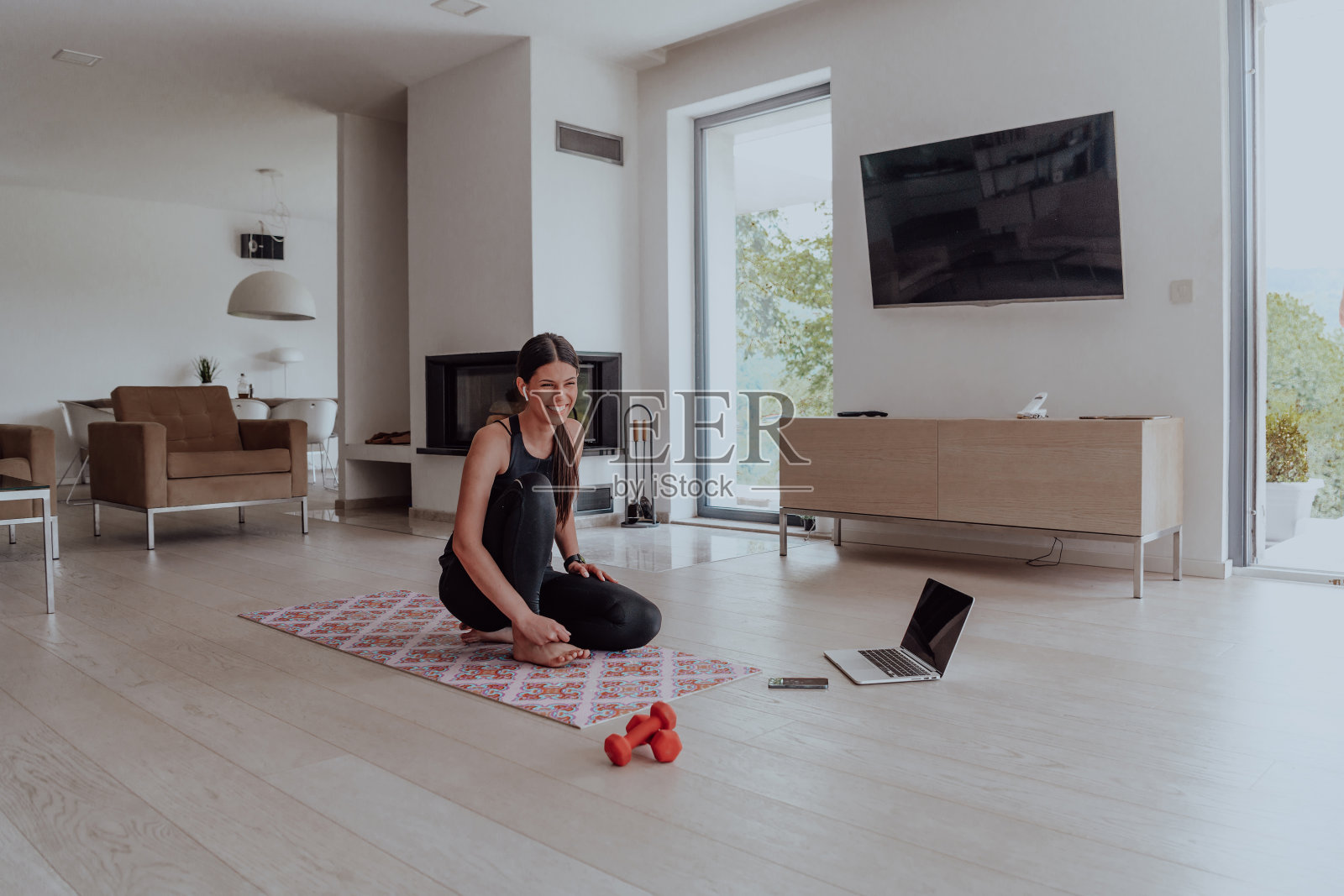 年轻美丽的女性锻炼，拉伸和练习瑜伽与教练通过视频电话会议在明亮阳光的阁楼公寓。健康的生活方式，幸福和正念概念。照片摄影图片