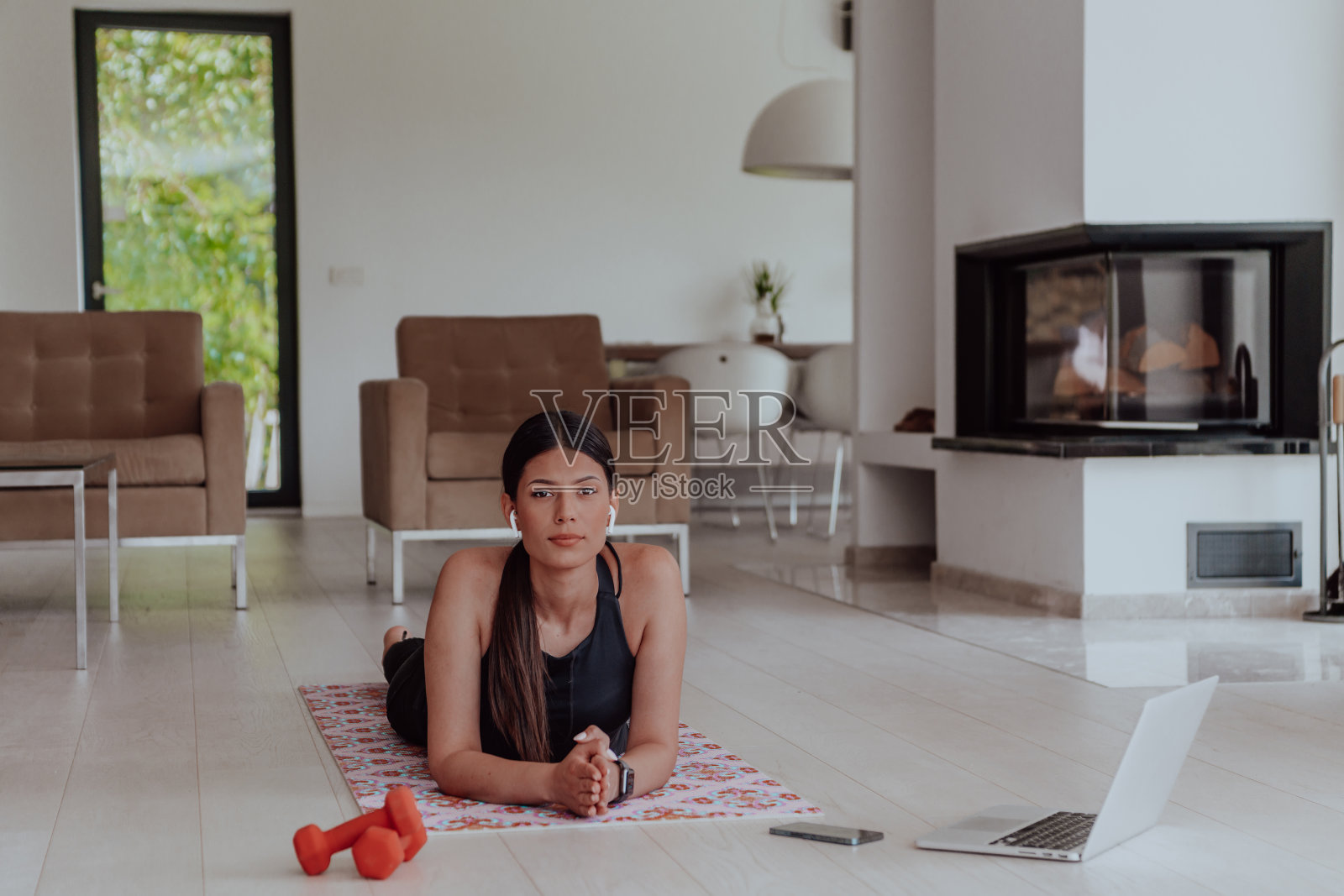 年轻美丽的女性锻炼，拉伸和练习瑜伽与教练通过视频电话会议在明亮阳光的阁楼公寓。健康的生活方式，幸福和正念概念。照片摄影图片
