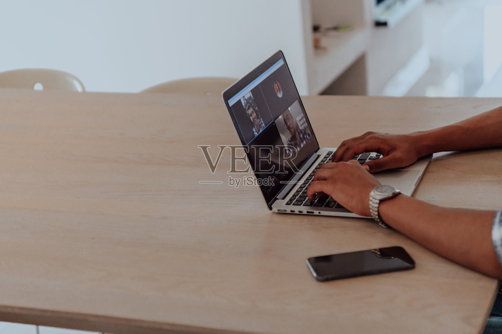 一名戴眼镜的非裔美国男子坐在现代客厅的一张桌子旁，用笔记本电脑进行商务视频聊天，与朋友交谈和娱乐照片摄影图片