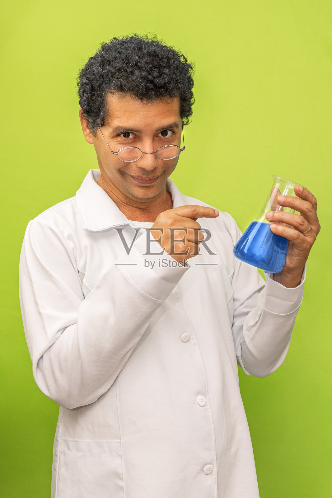 带着神秘微笑的天才科学家拿着并指着在绿色背景上做有趣的人脸肖像实验照片摄影图片