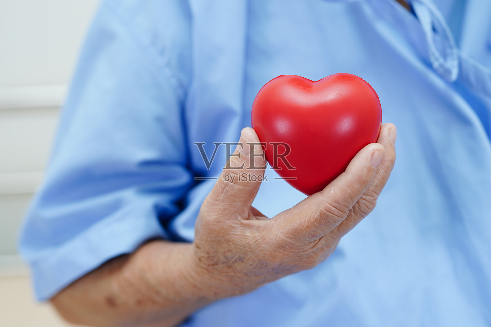 亚洲老年妇女病人在医院抱着红心。照片摄影图片