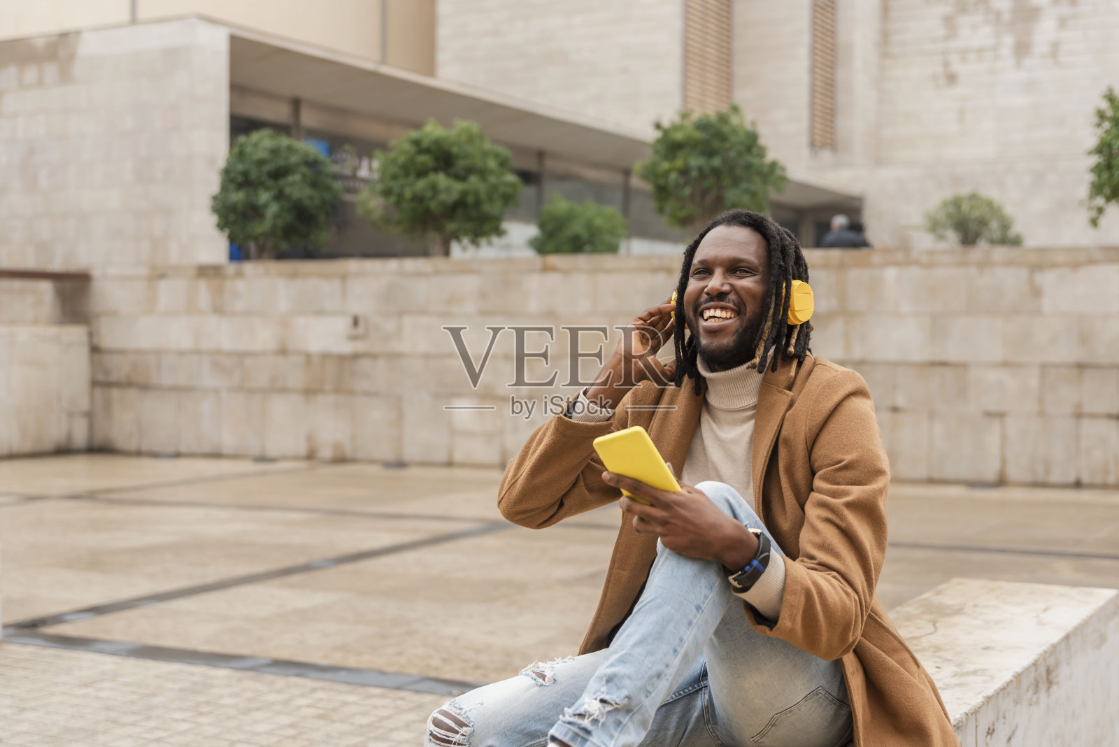 快乐的人用手机戴着黄色耳机听音乐坐在户外的城市照片摄影图片