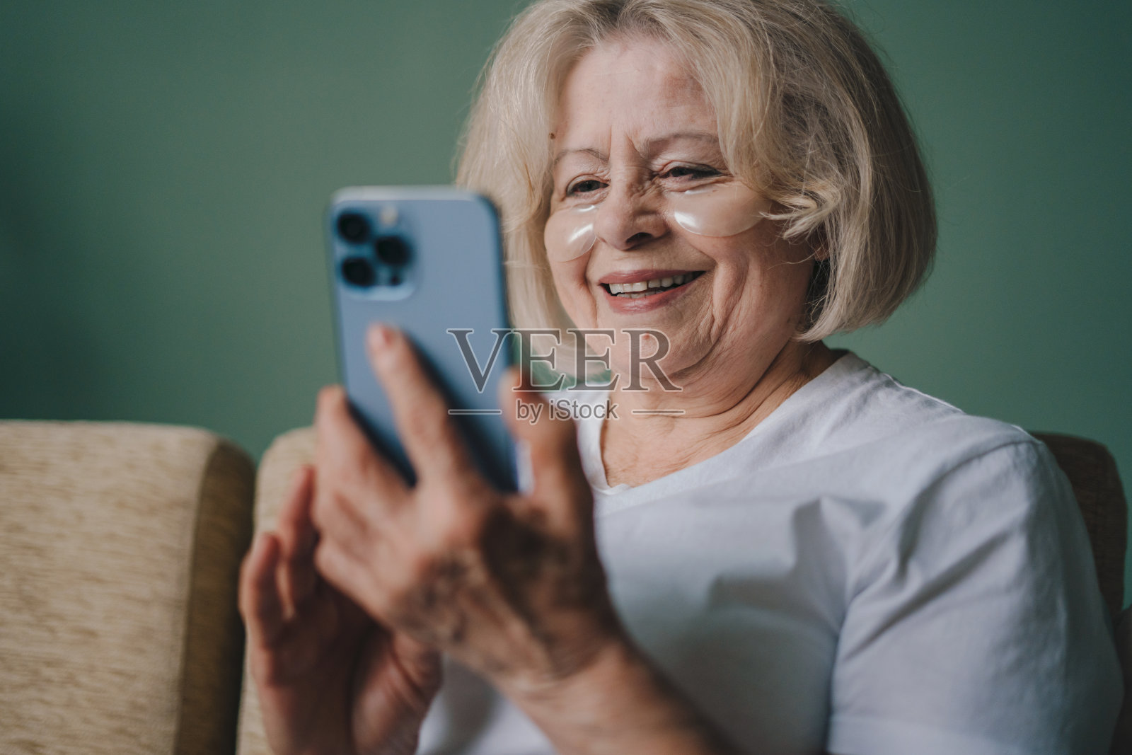 放松快乐的老年妇女眼罩使用手机，坐在家里的沙发上，享受在网上商店购物。在线交流概念。现代的老年人。放松，生活方式的概念。互联网通信。技术的概念。照片摄影图片