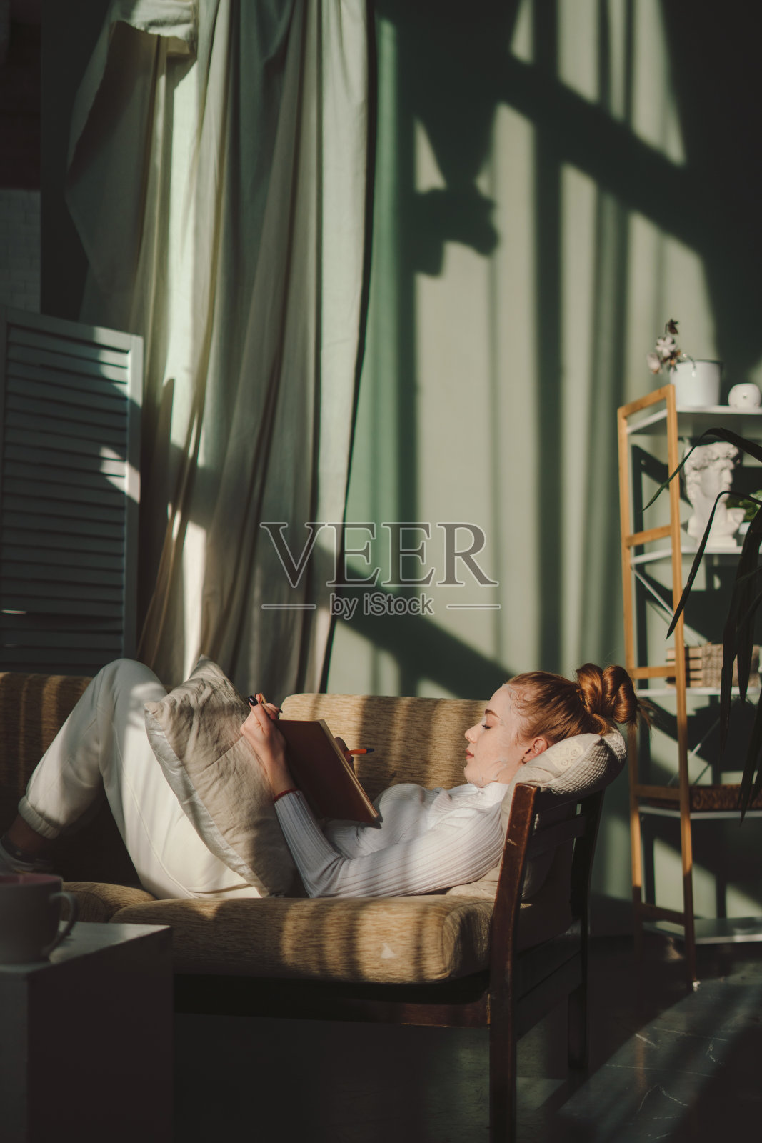 创意写作的女人在日记中做笔记，同时给自己一个面膜躺在沙发上的早晨。放松的女性计划，享受自由时间和平静的爱好照片摄影图片