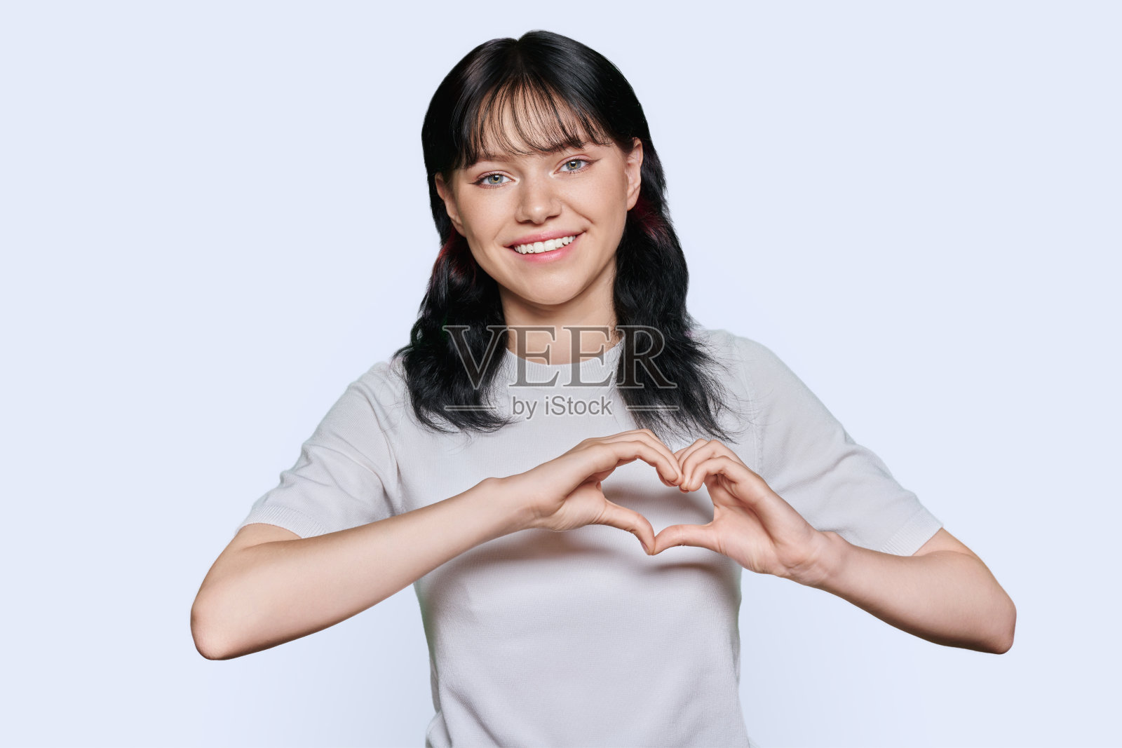 微笑的少女用双手在白色背景上展示心脏照片摄影图片
