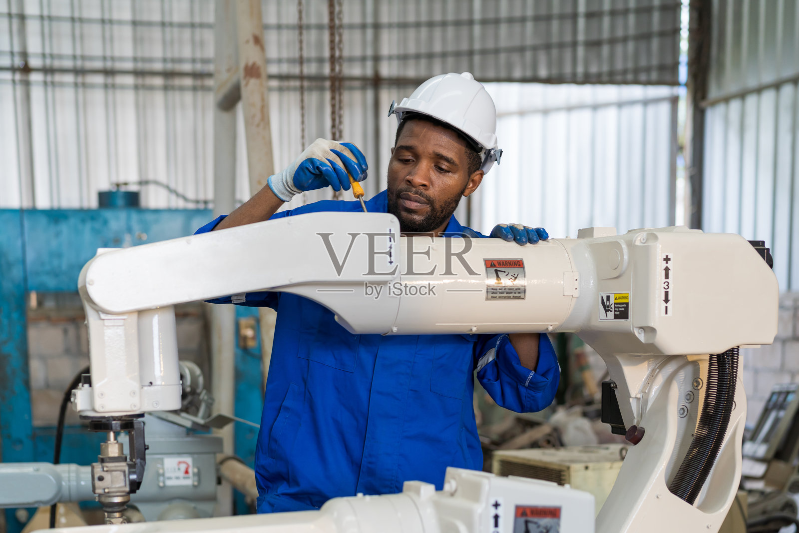 工厂男工程师在车间熟练操作机械臂。男性工程师在工厂维护自动机械臂机器。工业机器人制造技术照片摄影图片