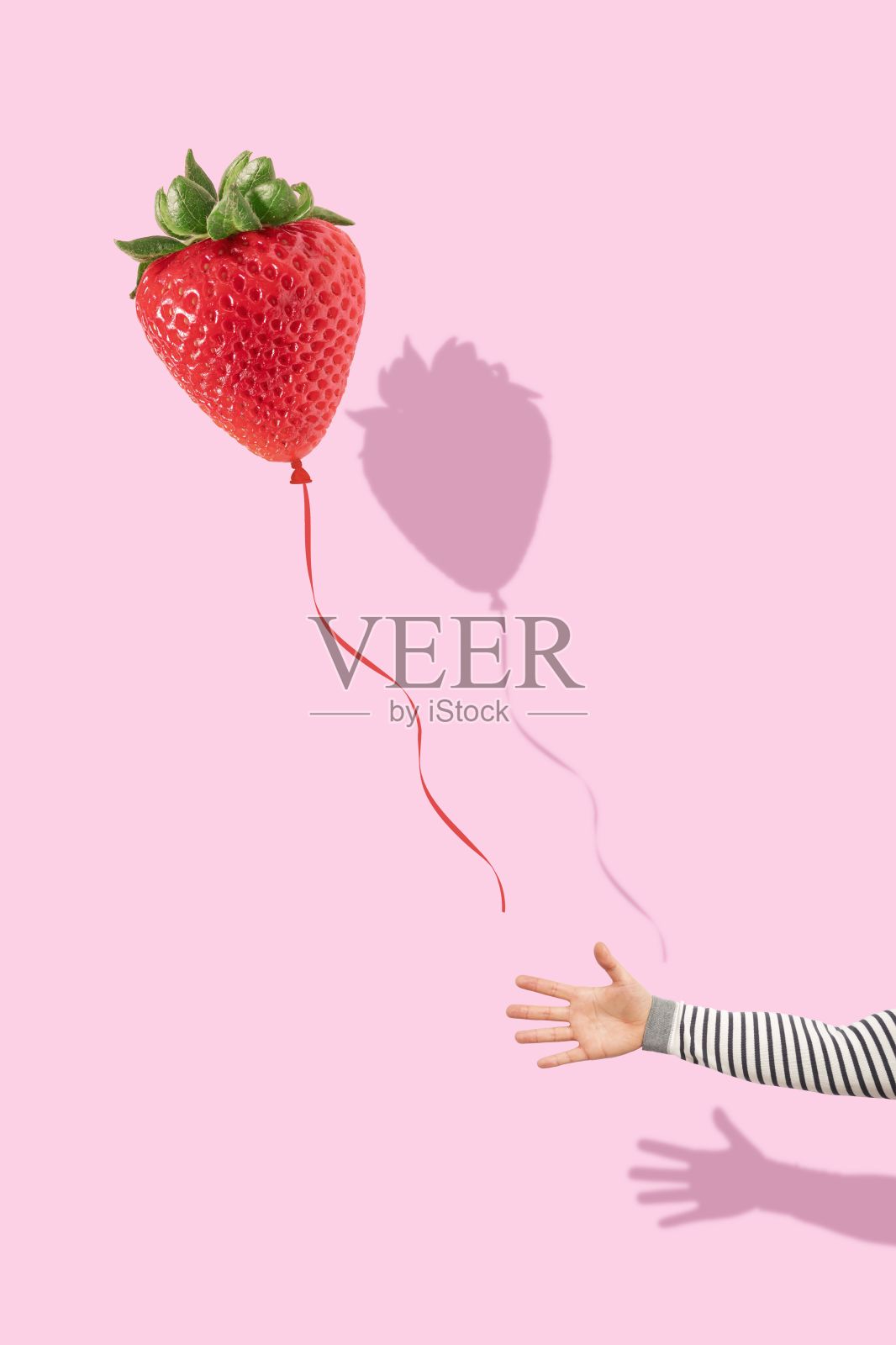 一只手在亮粉色背景上抓着一个红色草莓气球的垂直镜头照片摄影图片