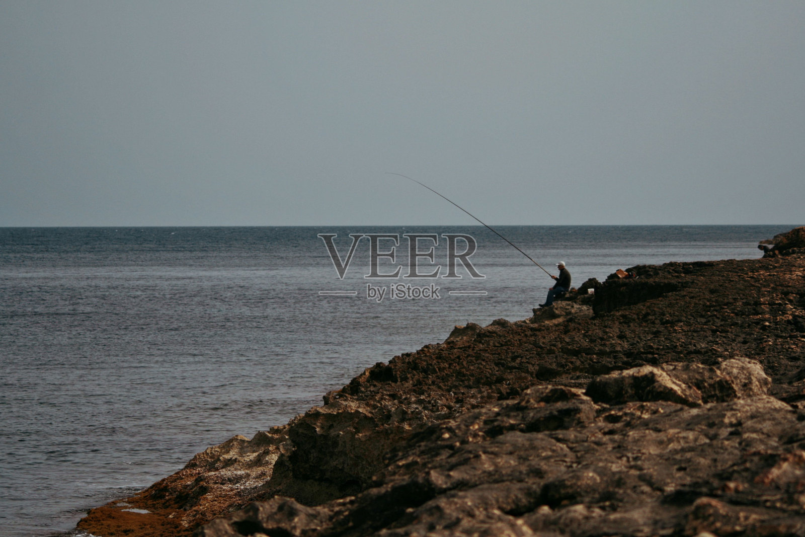 美丽的自然风光，一个孤独的渔夫坐在马耳他锯齿状的海岸上钓鱼照片摄影图片