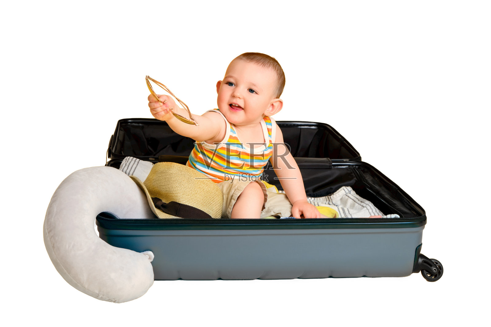 蹒跚学步的男孩坐在一个装有衣服的手提箱里，工作室孤立在白色背景上。一个孩子在为度假旅行打包行李时在一个大袋子里玩耍。一岁(12个月)照片摄影图片