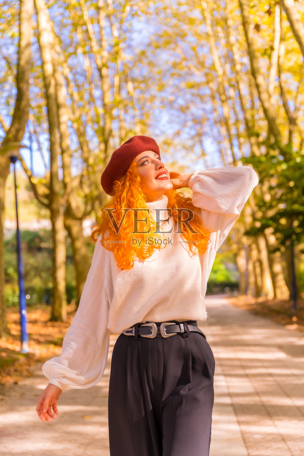 红头发的女人在贝雷帽走在城市森林公园在日落的肖像照片摄影图片