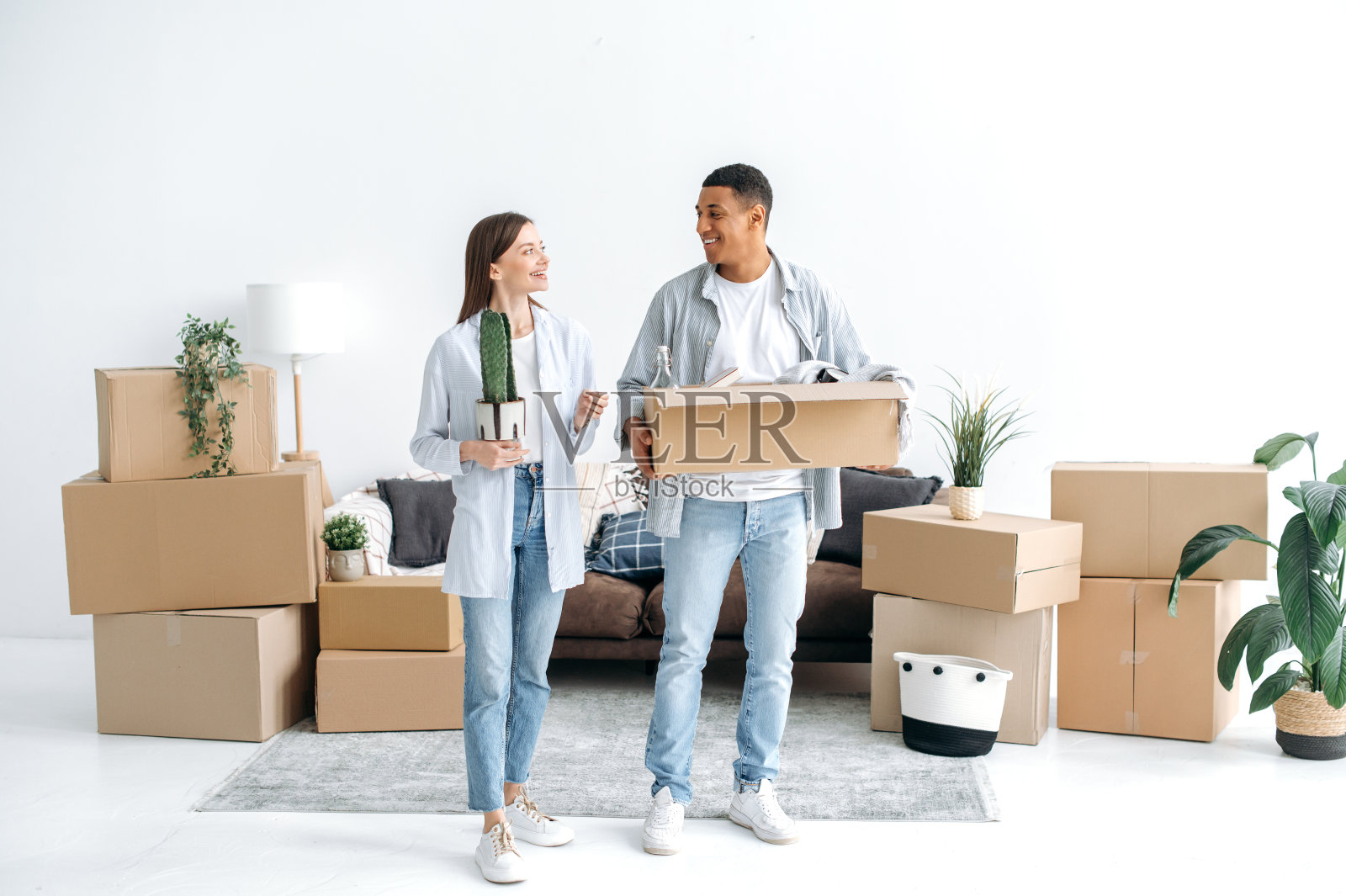 搬家的概念，购买房产。一对积极快乐的情侣，一个白种人女人和一个混血男人，站在他们的新家，在他们的新住处幸福地看着对方照片摄影图片