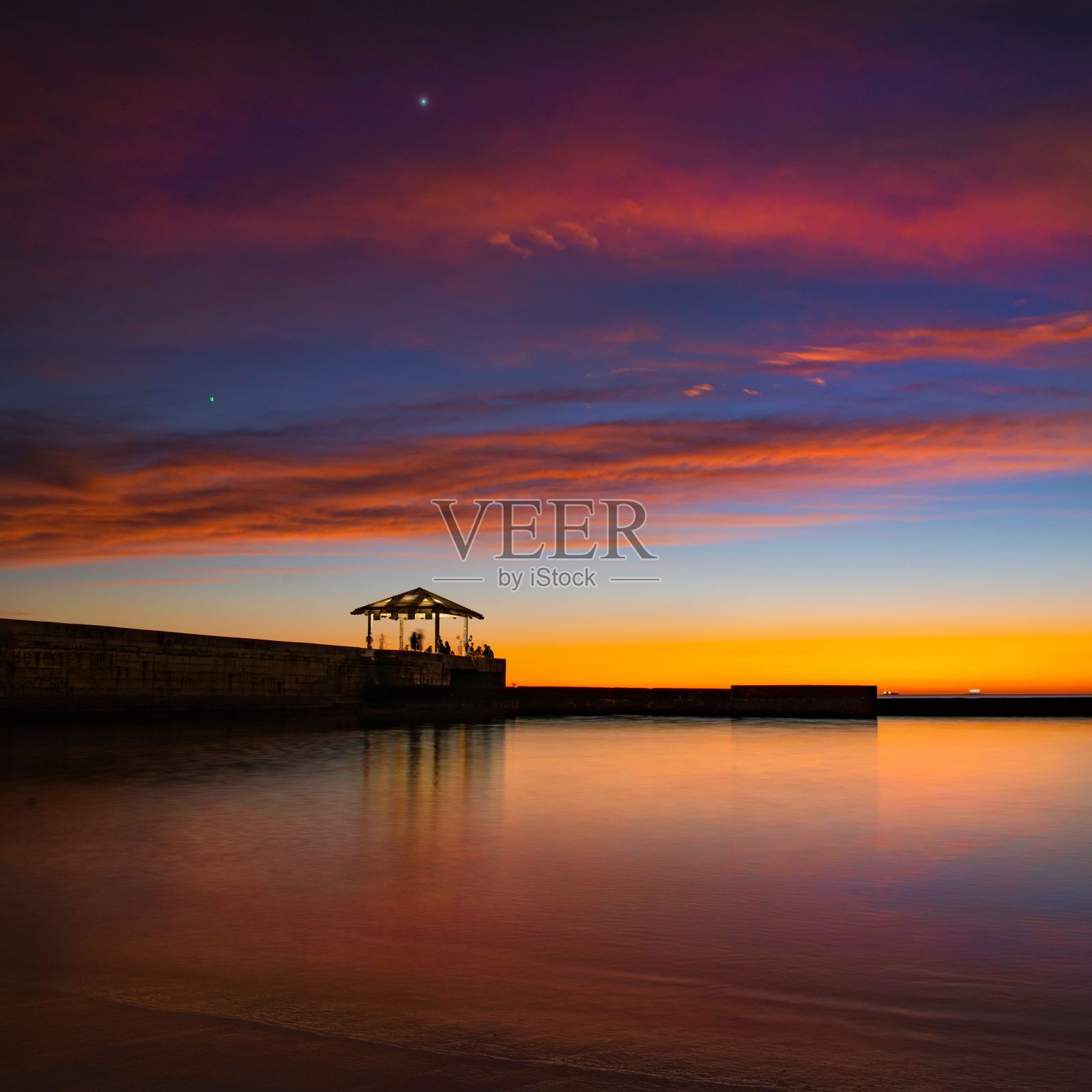 日落时分，海滩上的木板路和小屋，背景是绚丽多彩的多云天空照片摄影图片