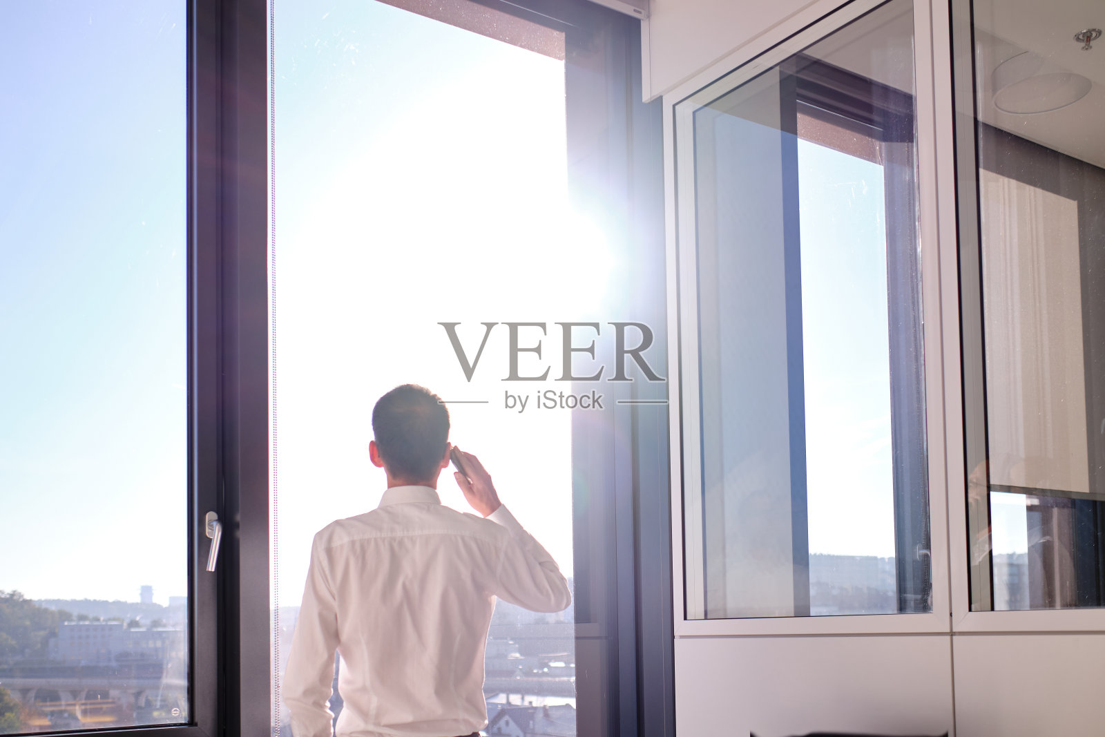 商务环境——商务人士站在办公室靠窗用手机打电话照片摄影图片