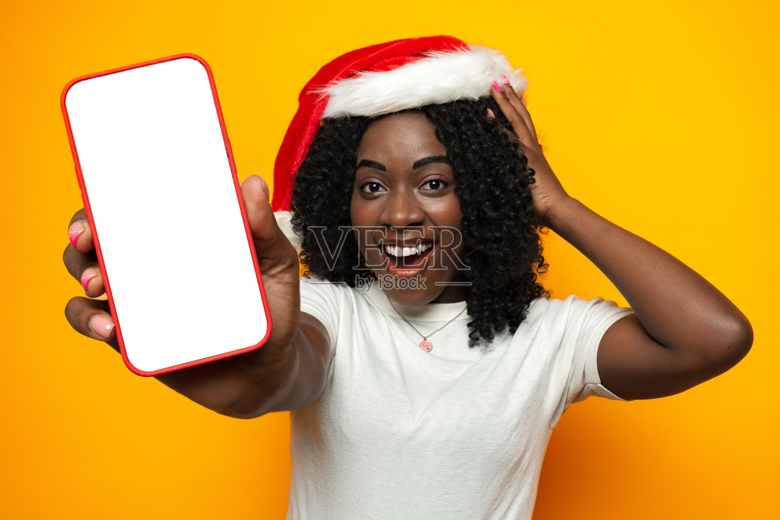 美丽的非洲女人戴着圣诞老人帽子，手机上有空白的copyspace屏幕照片摄影图片