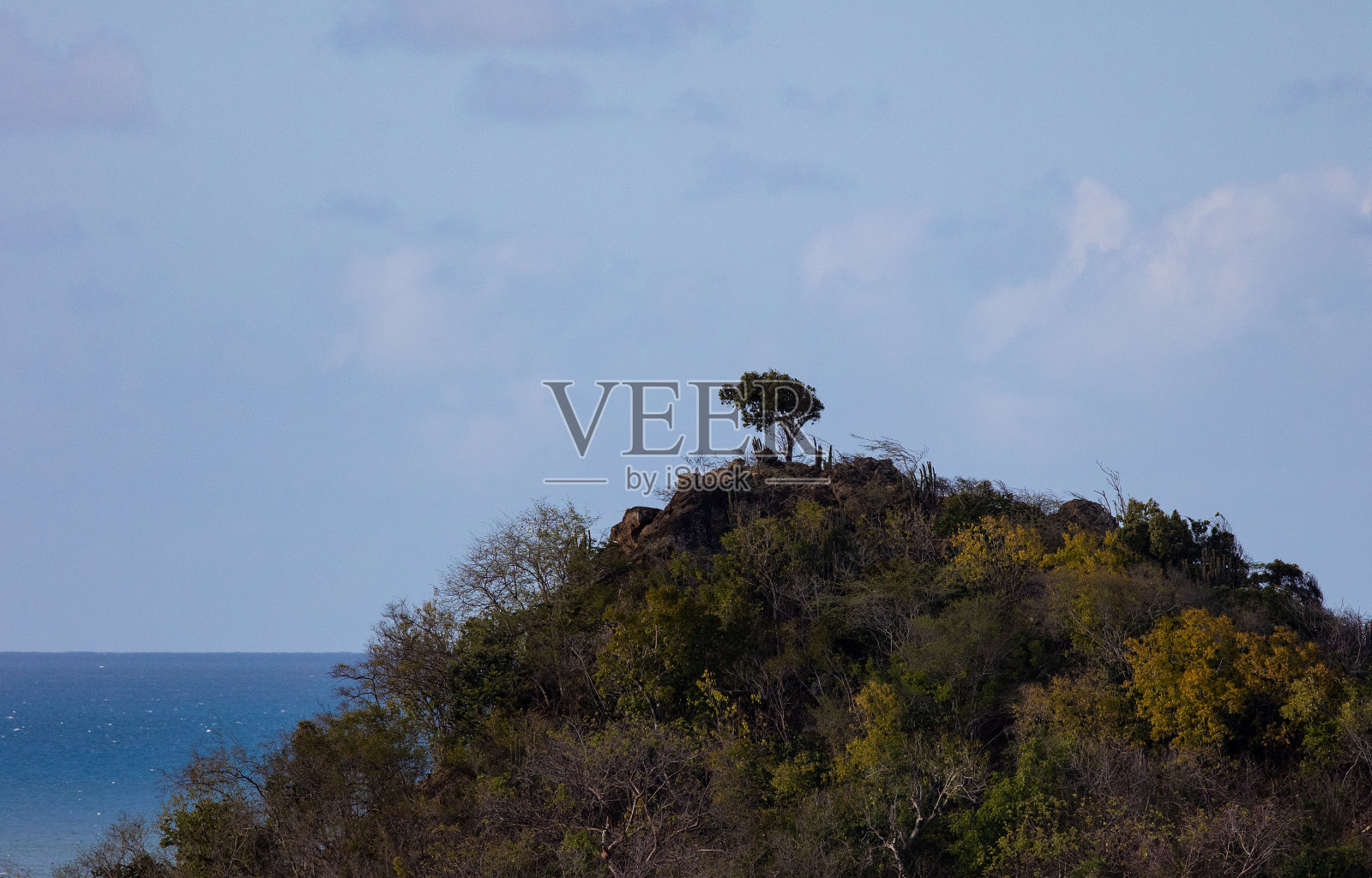 美丽的镜头，在多云的蓝天下，一座被绿草覆盖的山在大海前面照片摄影图片