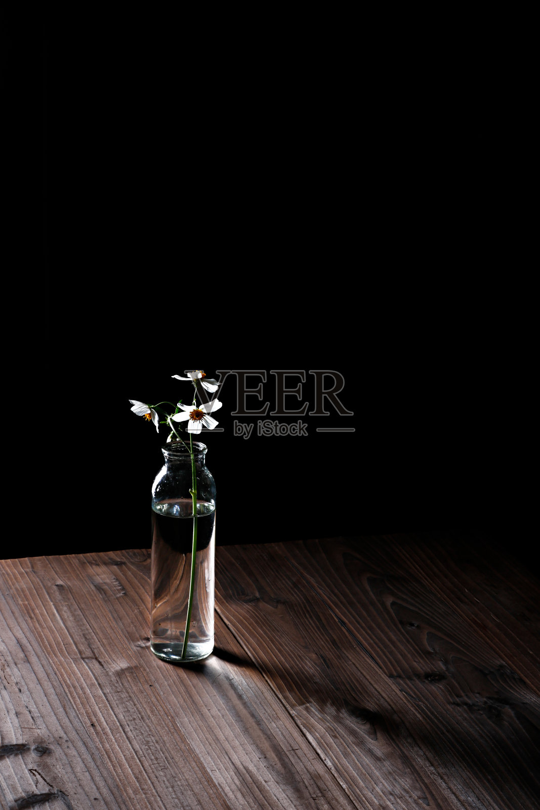 垂直特写的透明花瓶在木桌上对着黑暗的背景照片摄影图片