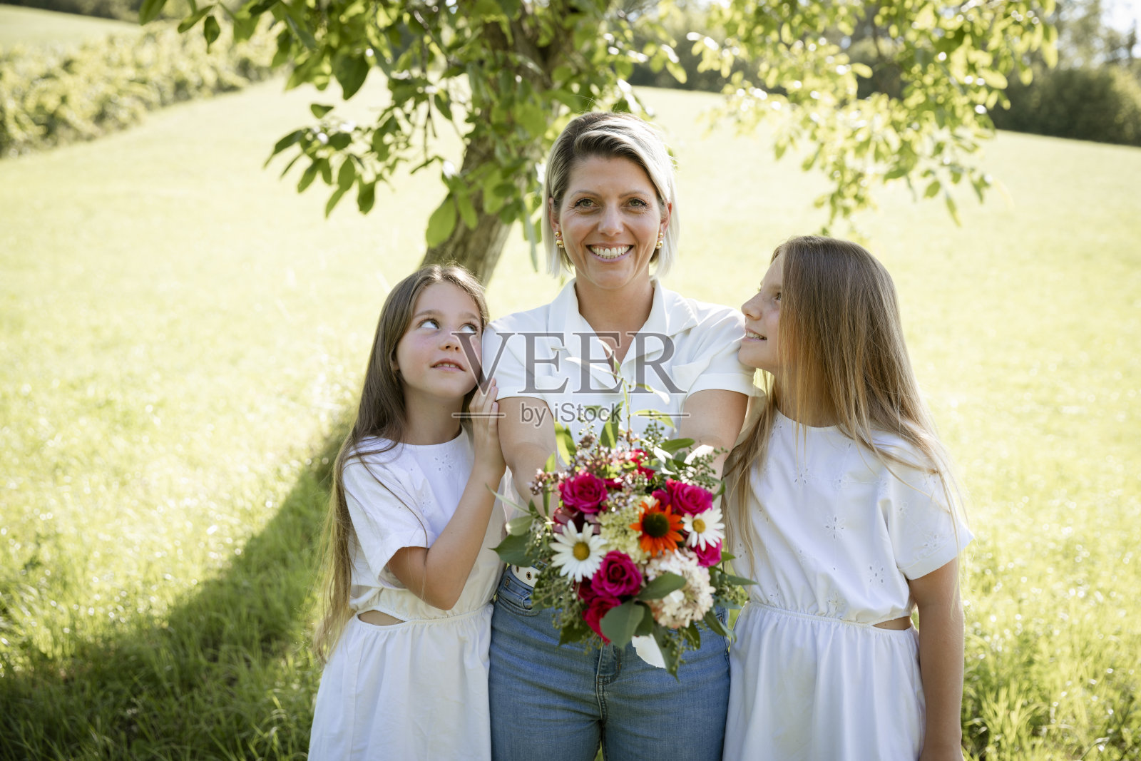 漂亮年轻的金发妈妈得到一束花从她的两个女儿的母亲节，生日，情人节照片摄影图片