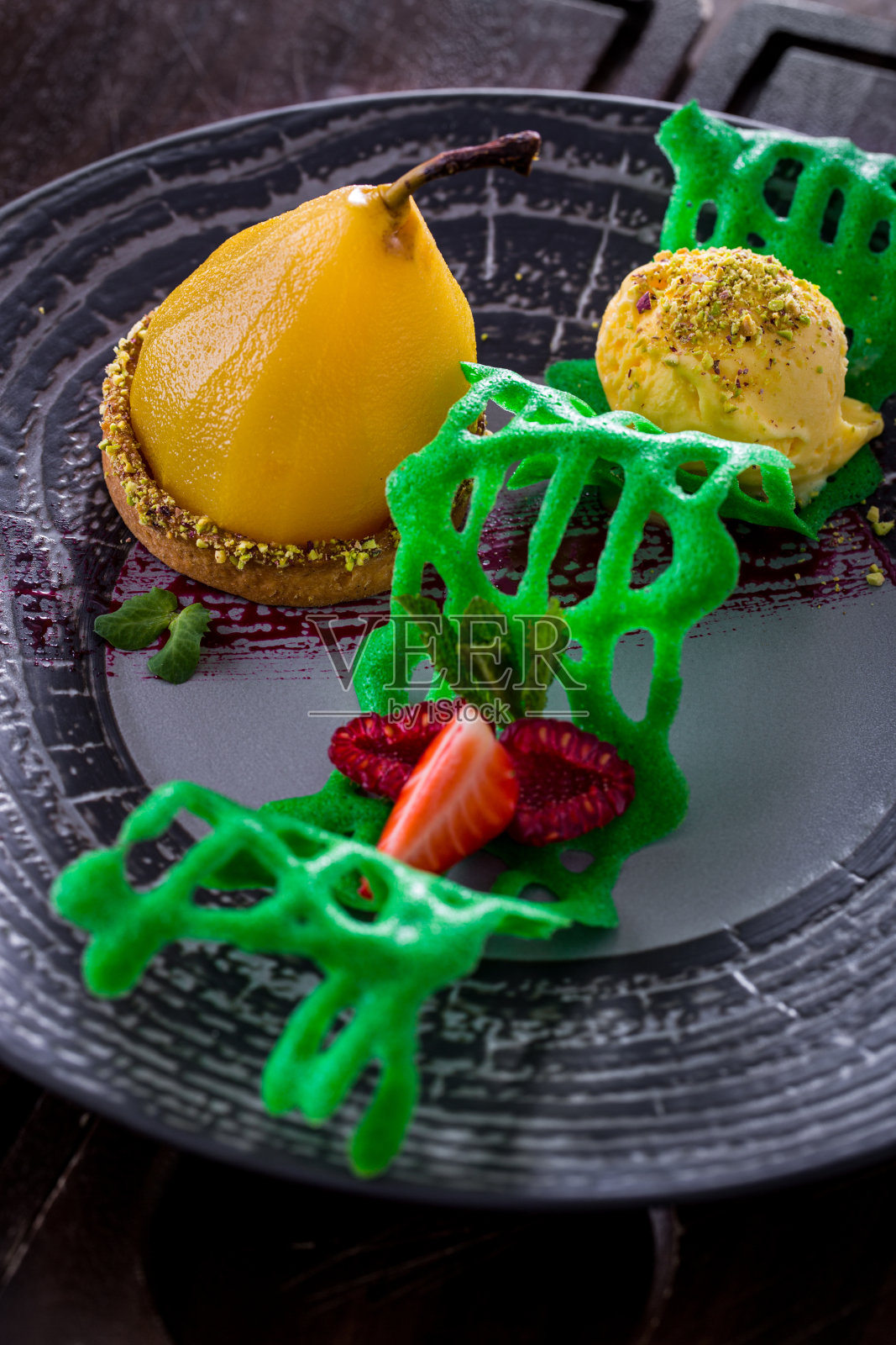 灰色盘子里的甜点蛋挞，里面有一整只梨、一团冰淇淋、草莓、覆盆子和绿色糖霜。垂直方向照片摄影图片