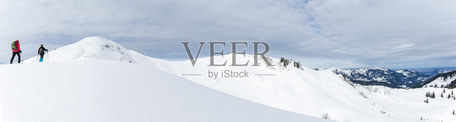 Senior couple is snowshoe hiking in alpine snow winter mountains panorama. Allgäu, Bavaria, Germany.照片摄影图片