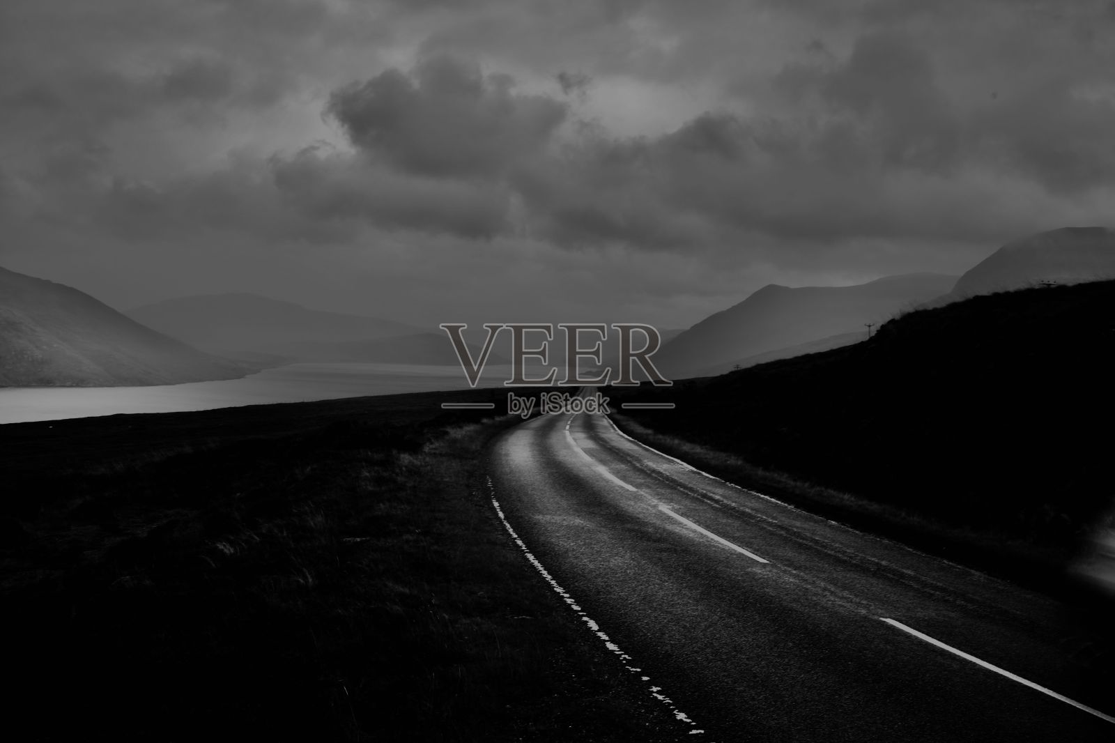 灰色的道路被田野包围，通往岩石光滑的山脉照片摄影图片