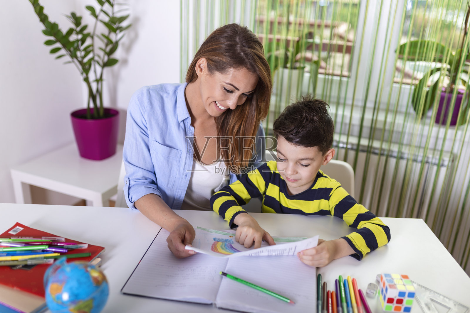 妈妈在帮小男孩做作业。冠状病毒大流行期间的在家上学。可爱的男孩和妈妈一起做作业，在家里，他正在书上写字照片摄影图片