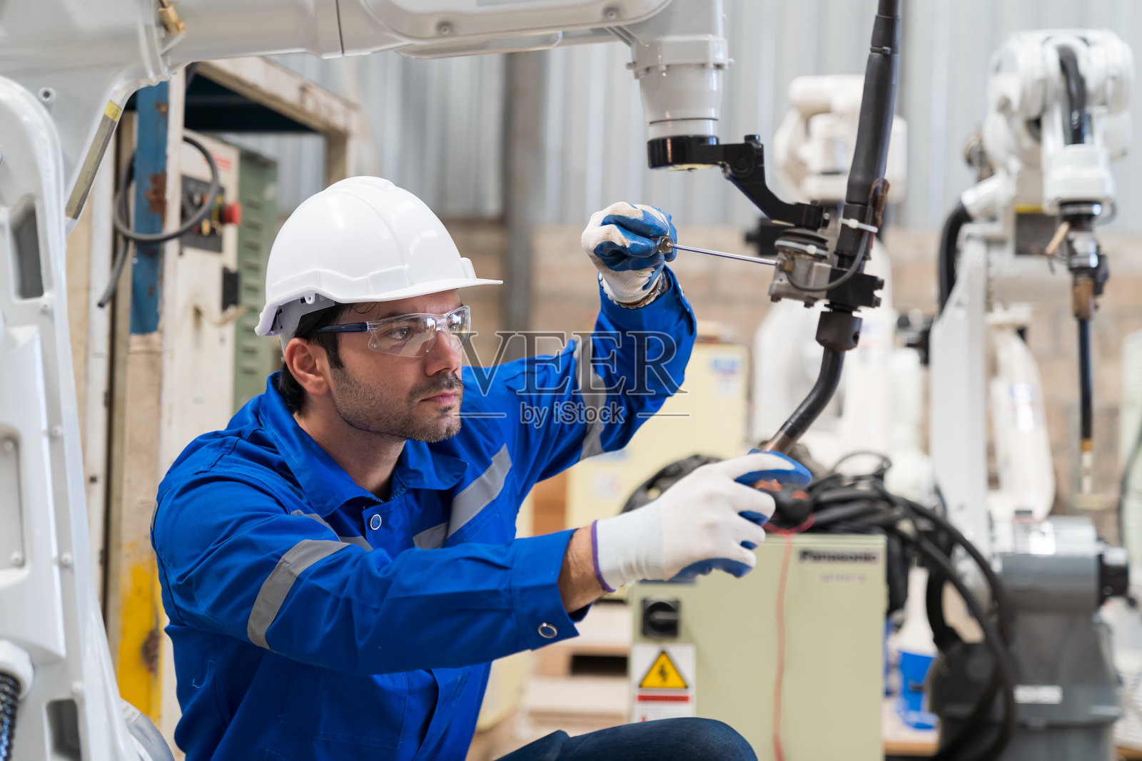 男工程师工人在工厂用螺丝刀维护自动焊接机械臂机。男技术员在生产线上检查、修理自动焊接机械臂机照片摄影图片