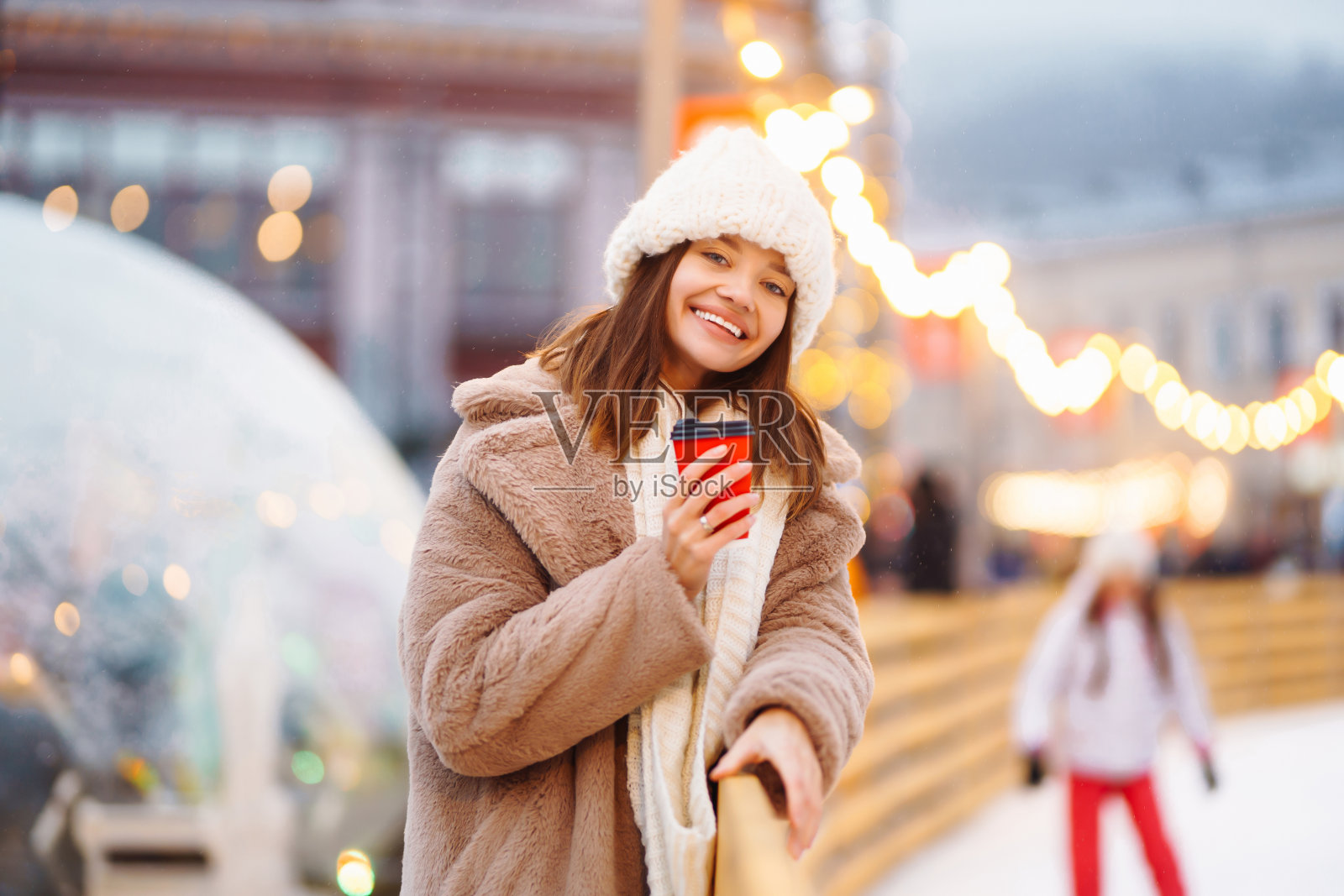 圣诞节，一个漂亮的女孩在集市上散步，喝着热饮。照片摄影图片