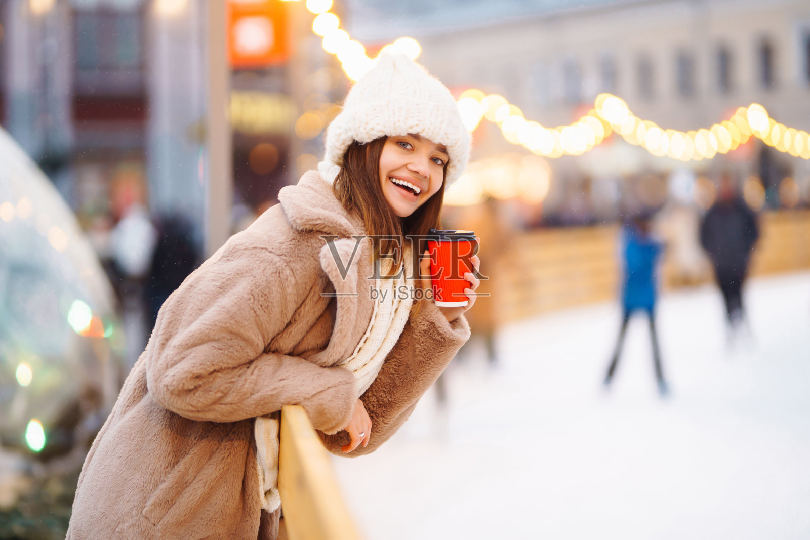 快乐的女人与一次性纸咖啡杯在冬天在户外溜冰场的背景。照片摄影图片