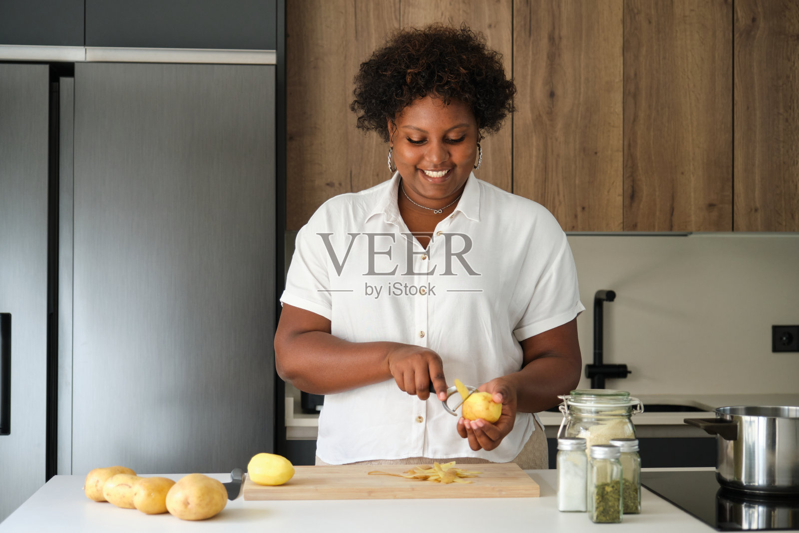 微笑的年轻古巴妇女剥生土豆。照片摄影图片