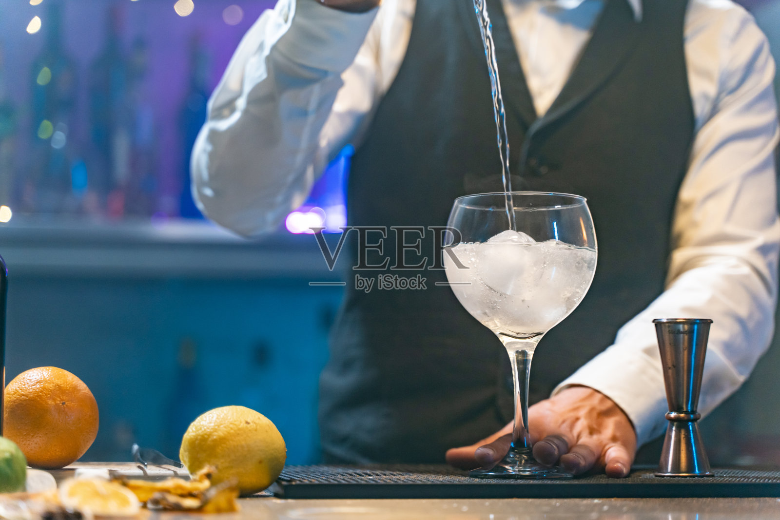 在夜总会的派对上，穿着白衬衫和黑围裙的难以辨认的酒吧服务员正在调制鸡尾酒。夜生活。照片摄影图片