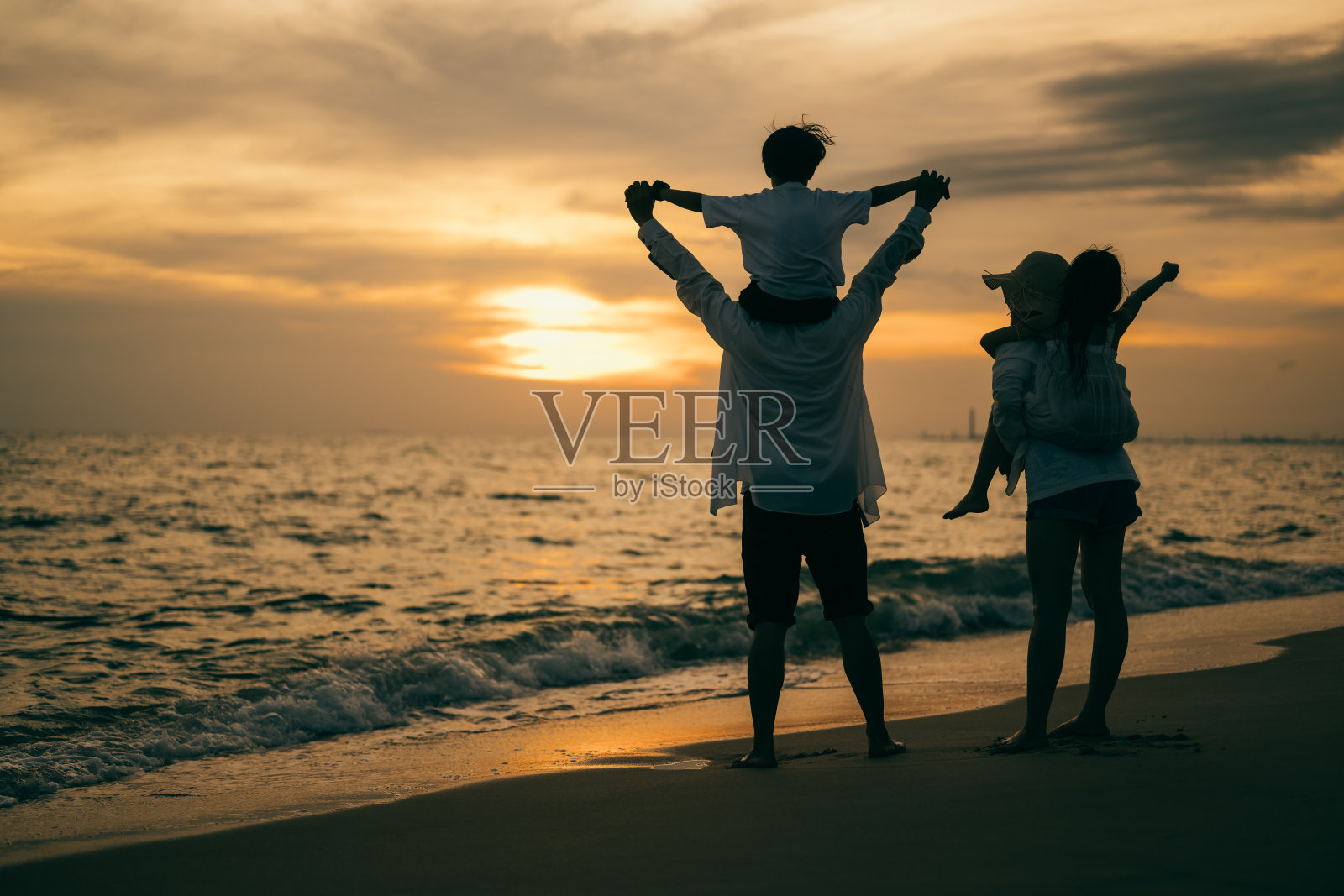 家庭剪影与海滩治疗，快乐的家庭一起花时间在海滩上，父母给孩子背在海滩上，日落的海滩上旅行，家庭度假和旅游的概念照片摄影图片