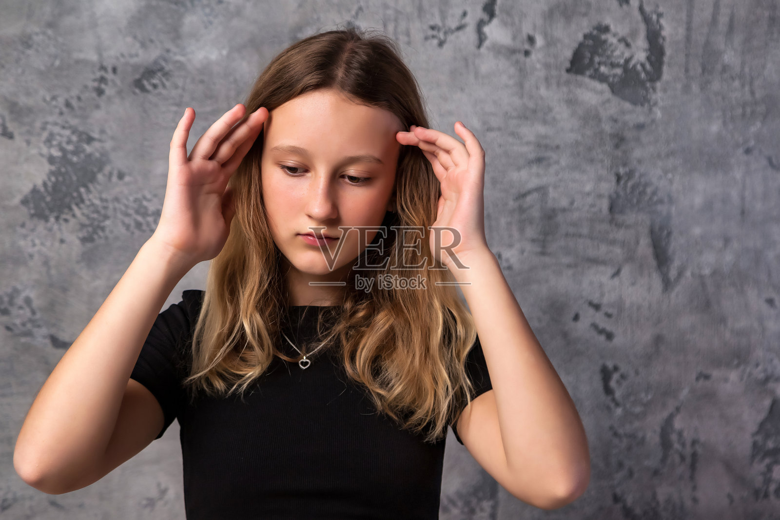 愁眉苦脸的少女穿着黑色的衣服，看着灰色的背景，沉思着。沉思周到的少年女孩12岁在工作室摆姿势。儿童情感概念。复制文本空格照片摄影图片