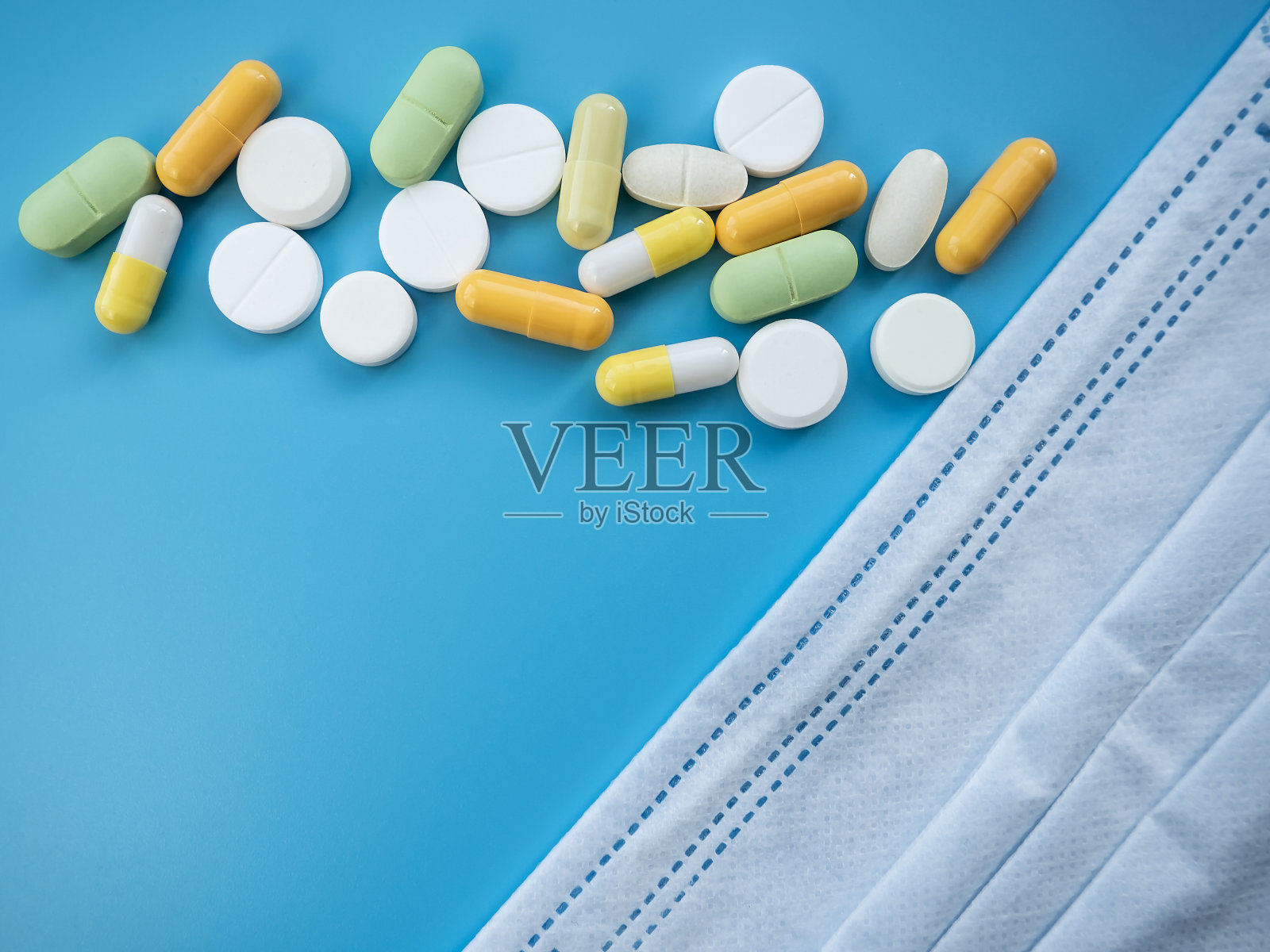 蓝色背景的药丸和医用口罩。医疗制剂、片剂、胶囊和维生素。医药抗生素。医学、保健的概念。照片摄影图片