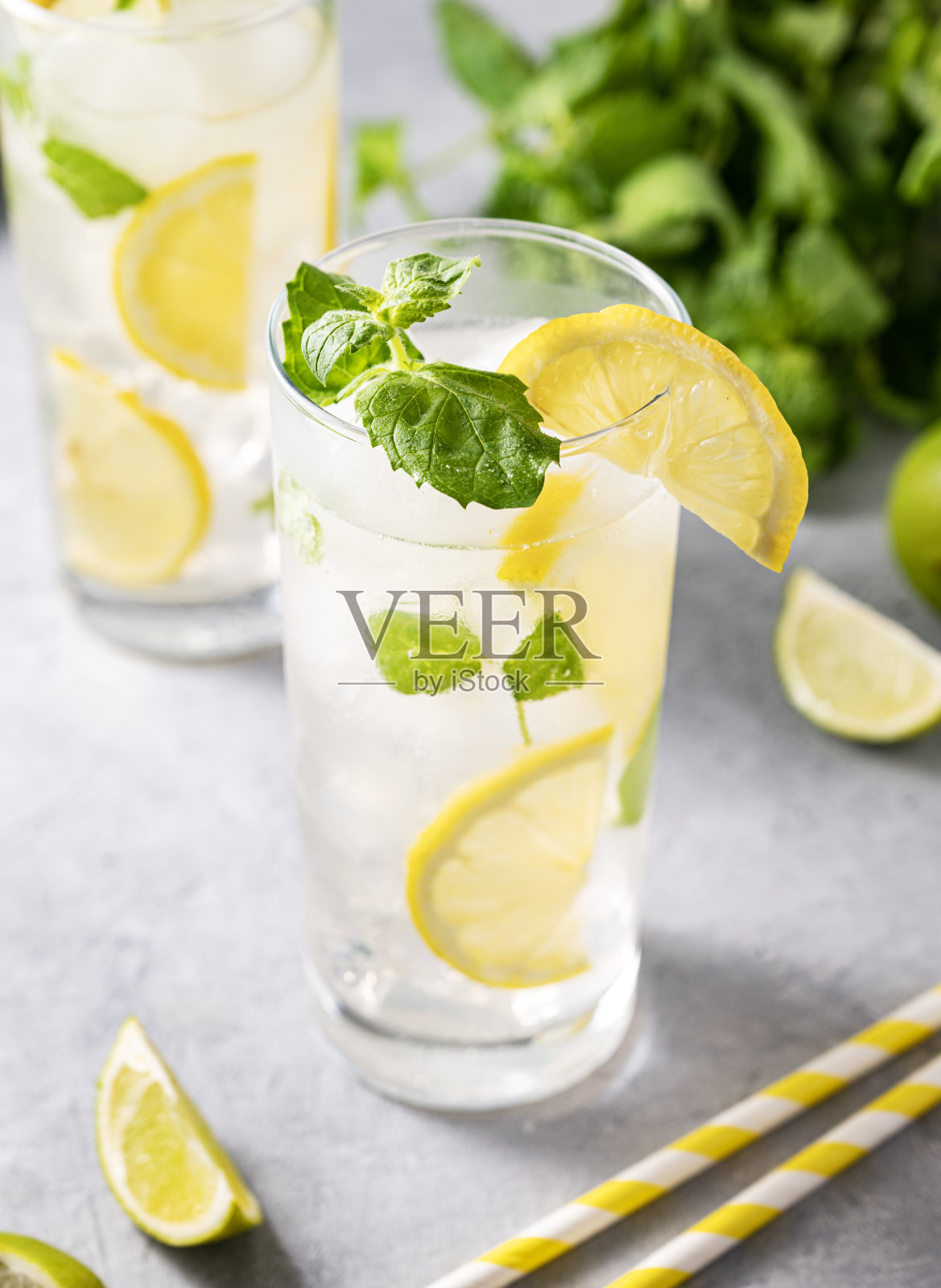 莫吉托加新鲜柠檬。用青柠、柠檬、薄荷和冰块调制的清爽鸡尾酒，倒入高脚杯，底色为灰色。照片摄影图片