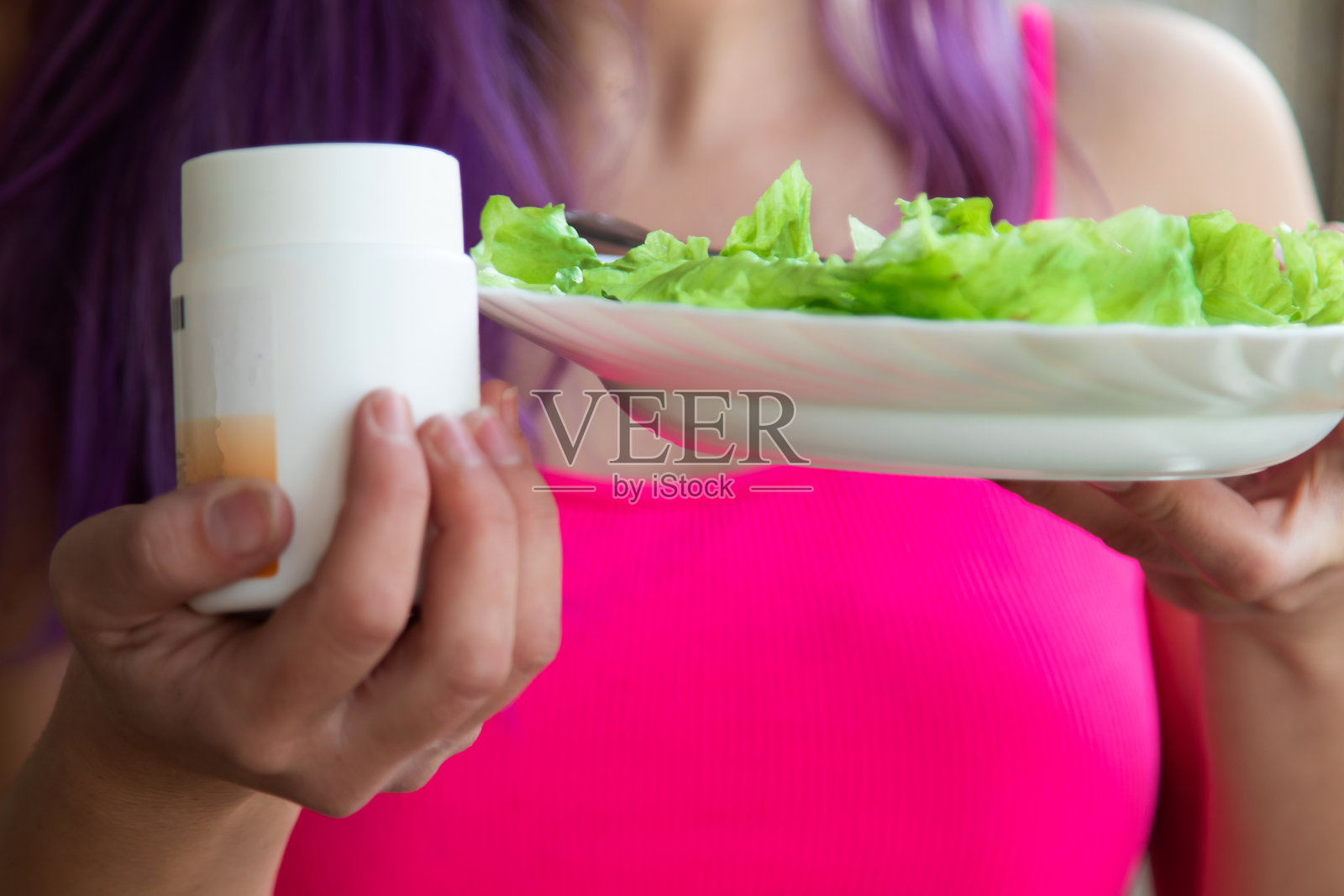 女人拿着一瓶营养补充剂和一盘生菜照片摄影图片