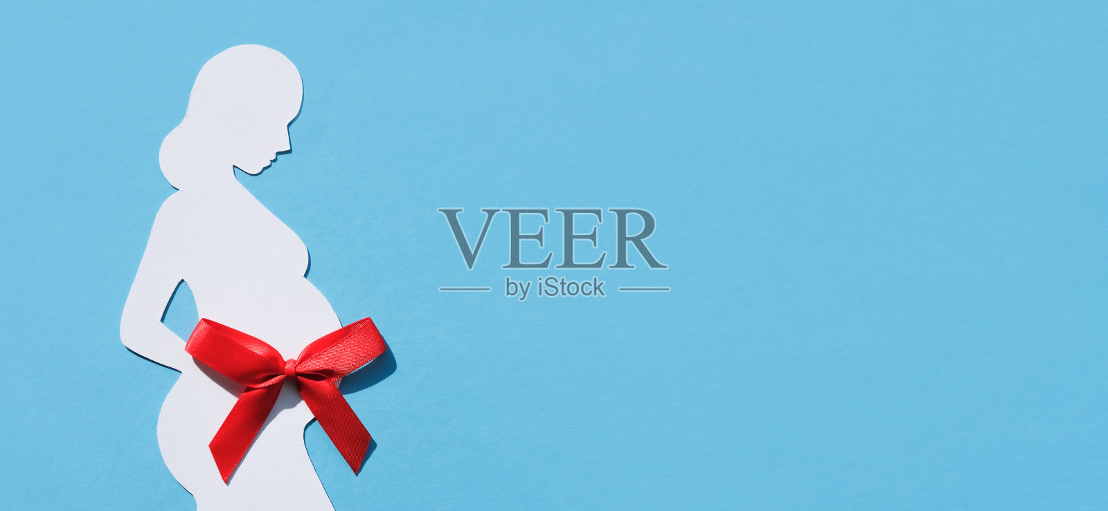 一个孕妇的剪影与红色蝴蝶结在她的肚子上的蓝色背景。横幅，平铺，文字的地方。健康母亲的概念。照片摄影图片