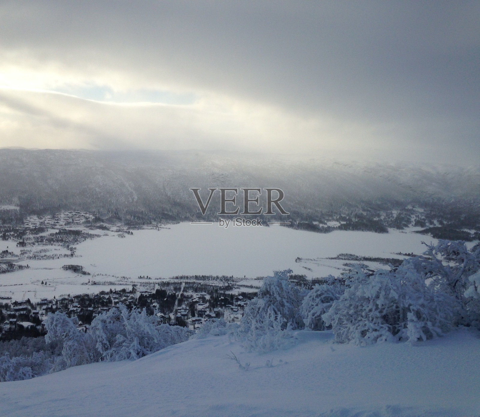 在多云的天空下，冬天结冰的湖被雪覆盖的风景照片摄影图片