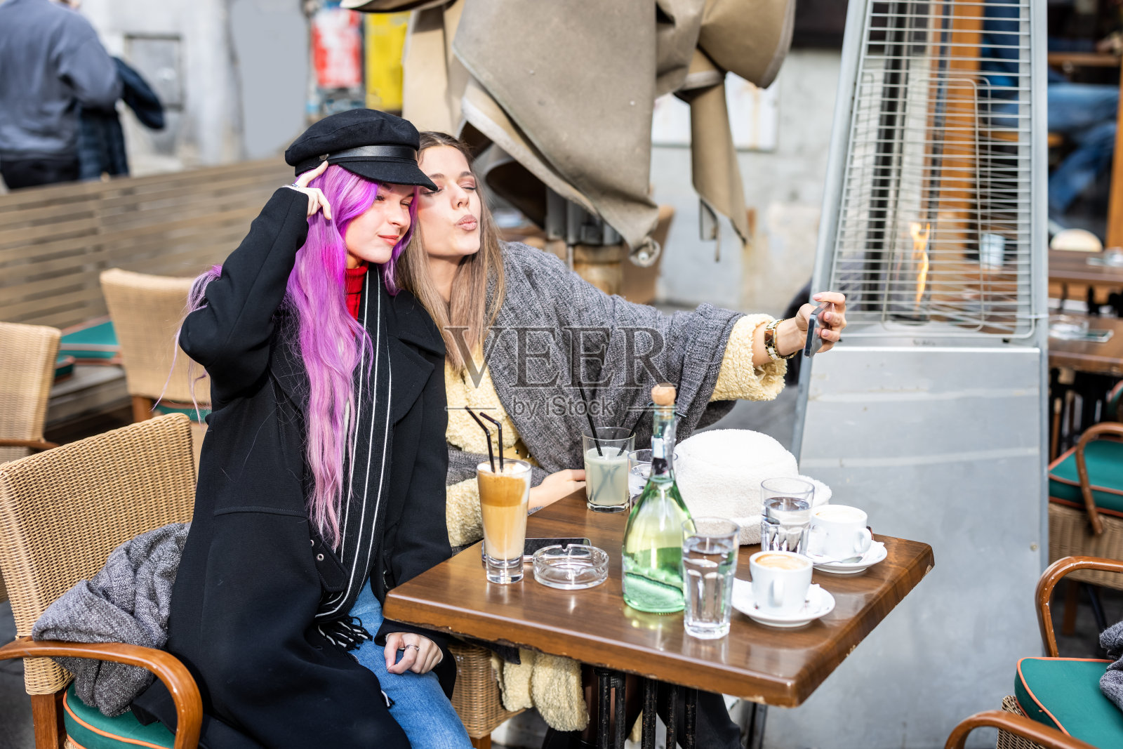 两个穿着暖和衣服的年轻女子坐在当地的咖啡馆里自拍。照片摄影图片