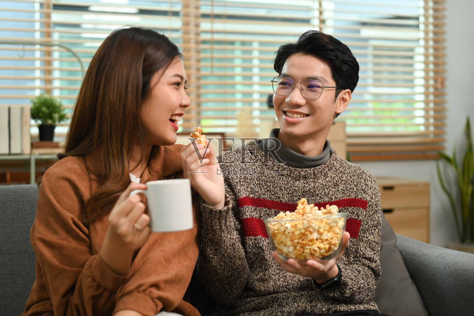 年轻幸福的夫妇拿着爆米花在家看电视的画面。休闲与人的理念。照片摄影图片